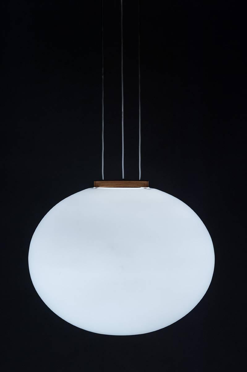 A beautiful pendant in oak and opaline glass by Uno & Östen Kristiansson for Luxus, Sweden.
The lamp is suspended by three wires from the canopy and divided by a piece of wood on the shade, creating a triangle of wires in between. The shade is made