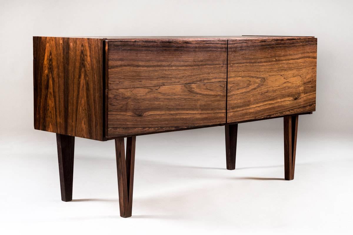 Gorgeous small sideboard manufactured in Sweden, possibly designed by Ib Kofod-Larsen.
This rare sideboard consists of two big drawers on the left side, with handles beautifully hidden on the top; and three smaller drawers hidden behind a flap door