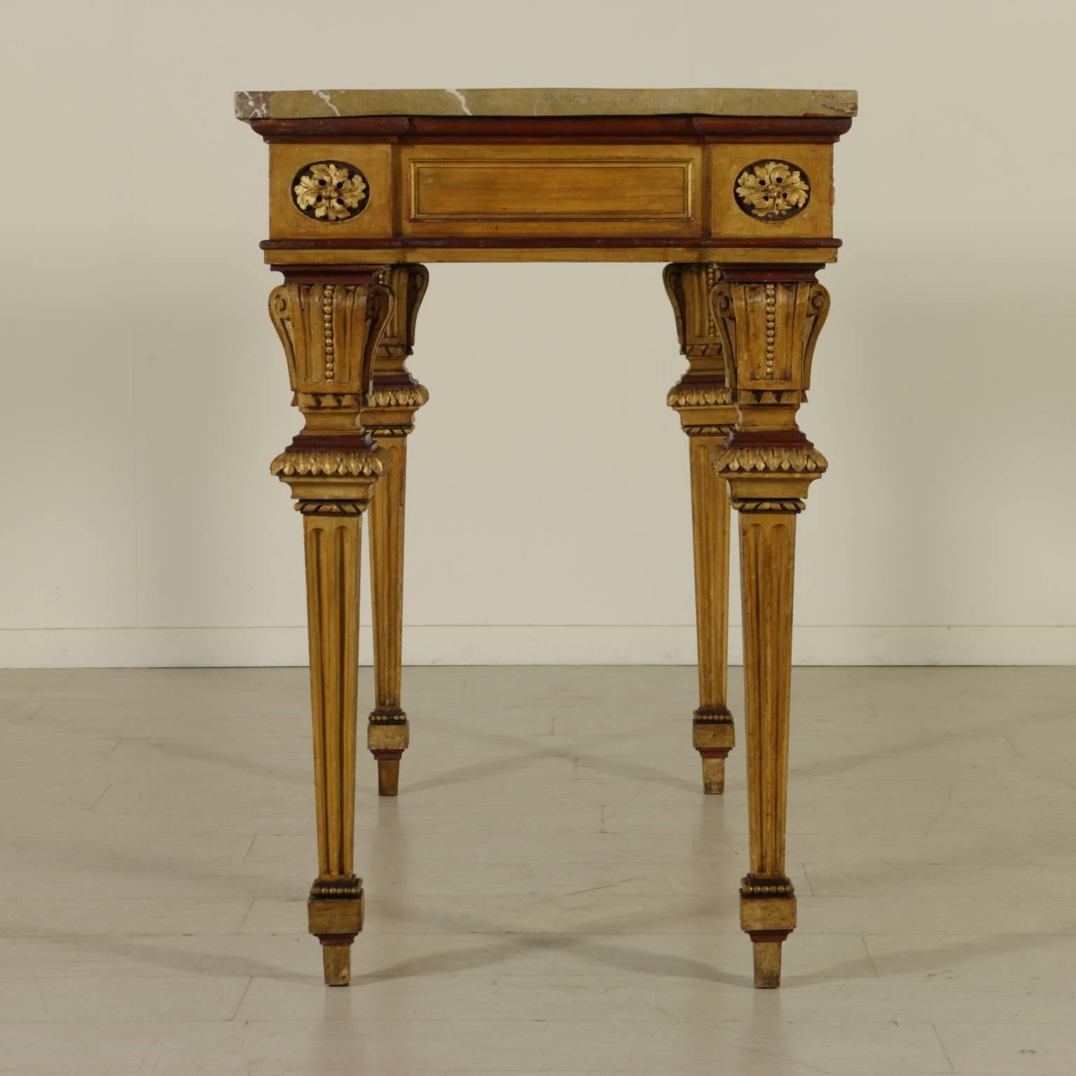 A neoclassical late 18th century lacquered wood wall table with truncated pyramid legs and carved shelves. Frames decorated with leaves, lion head and oak leaves roses. Macchiavecchia marble top. Gilded and lacquered. Manufactured in Northern Italy