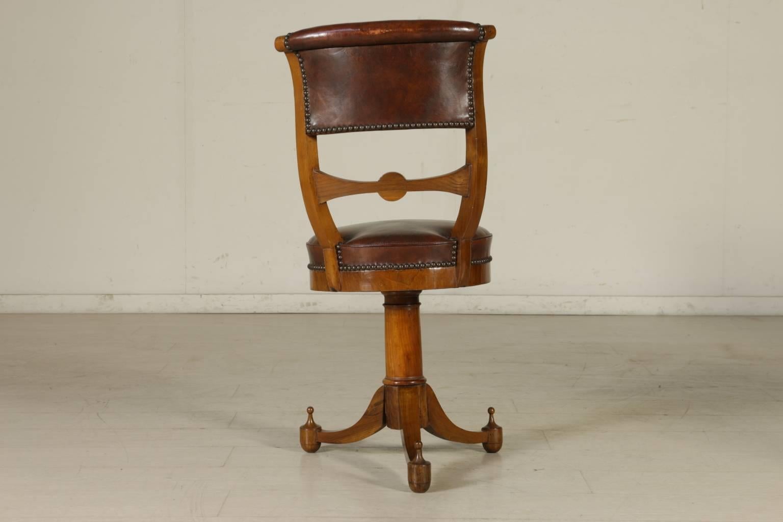 A group of four early 19th century Empire walnut and cherry music chairs with central baluster. Three turned legs ending in a tip. Round padded seats and padded open backrests. Imprinted and gilded leather seat and backrest with Napoleonic coat of
