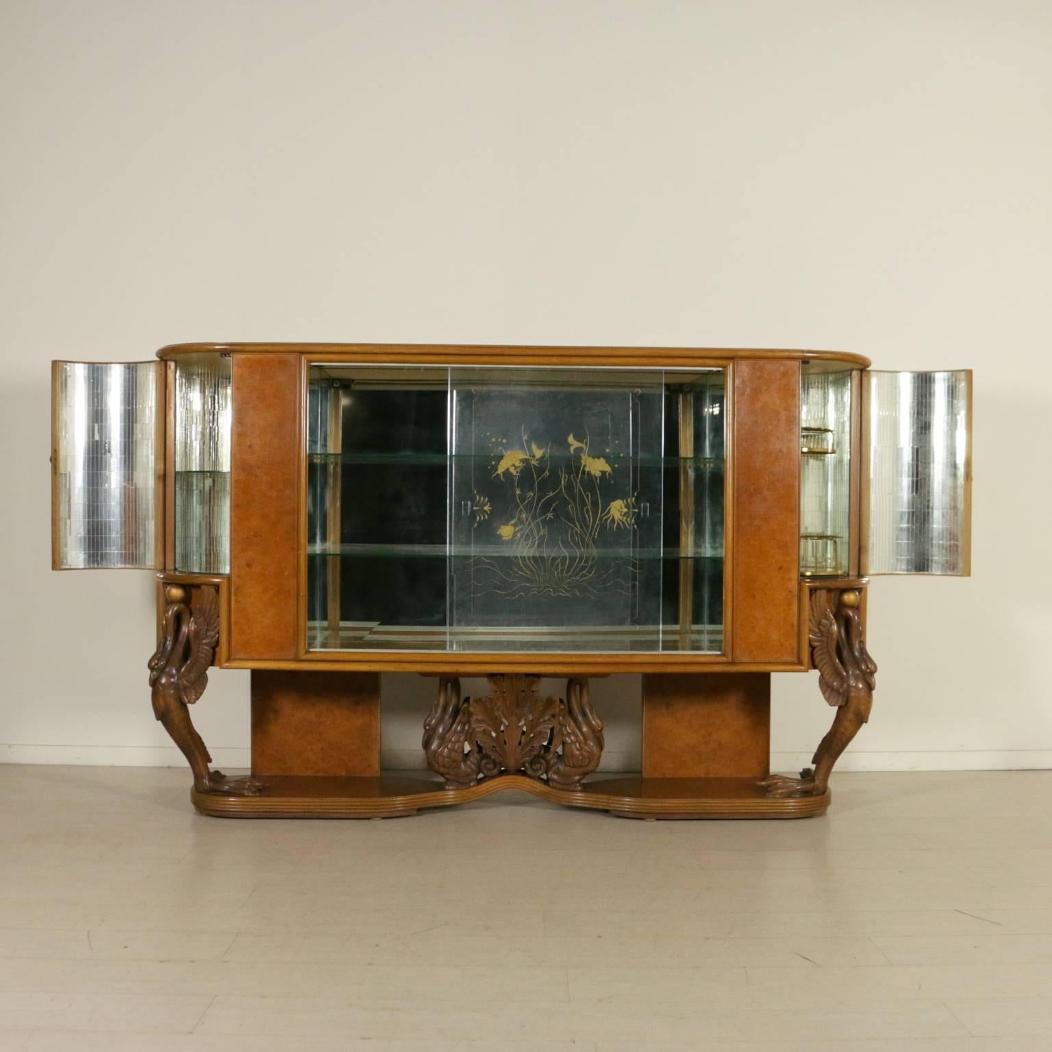 A showcase with decorated glass sliding doors, bar side compartments with bent doors. Burl veneer, carved wooden legs, brass handles. Manufactured in Italy, 1940s.