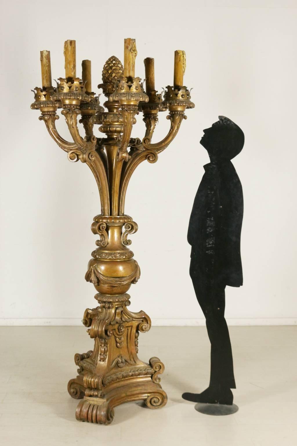 A large carved and gilded wooden torch holder, assembled with antique materials. Tripartite stand with neoclassical carvings and spirals. The central body ends in a carved pineapple and six arms with opposing C-shape, holding the lamps. Manufactured