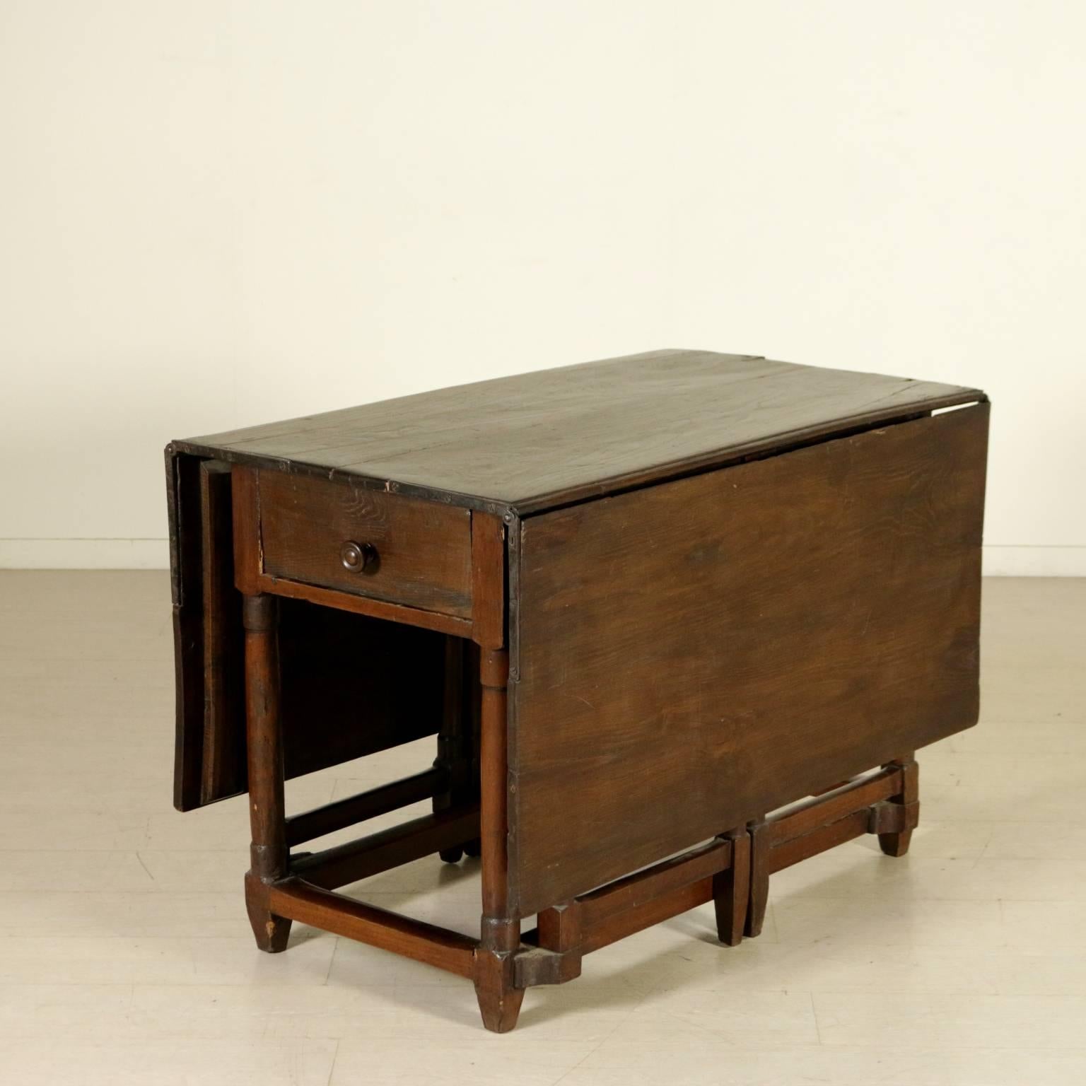 English oak drop flap table with turned legs joined by stretchers and a drawer in the front band. Wide drop flaps on the sides, hold by openable legs. Manufactured in England, 19th century.