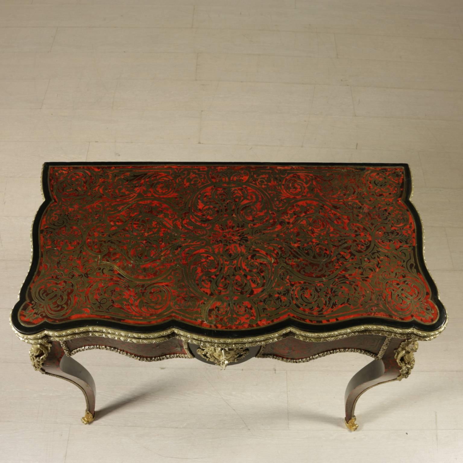A Boulle style richly inlaid game table with four curved legs, curved band, openable top. Ebony and red turtle inlaid surface, with engraved brass inlays. Green velcro inside the top. The table is enriched by glided bronzes surrounding all the
