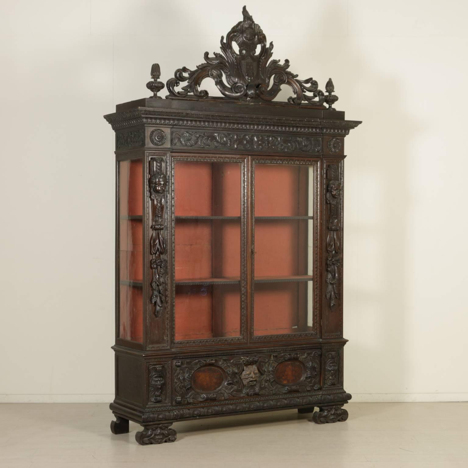 A pair of late 19th century Neo-Renaissance walnut bookcases with different carvings. Composed of various antique wood varieties. Two doors and sides with glasses. Richly carved with masks, pilasters with fruit, crest with coat of arms.