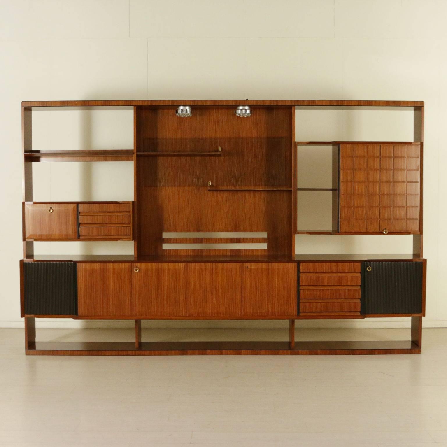 A living room cabinet with compartments, hinged doors, drawers, open shelves. Rosewood veneer, ebony stained and decorated panels, ceiling lamps. Manufactured in Italy, 1960s.