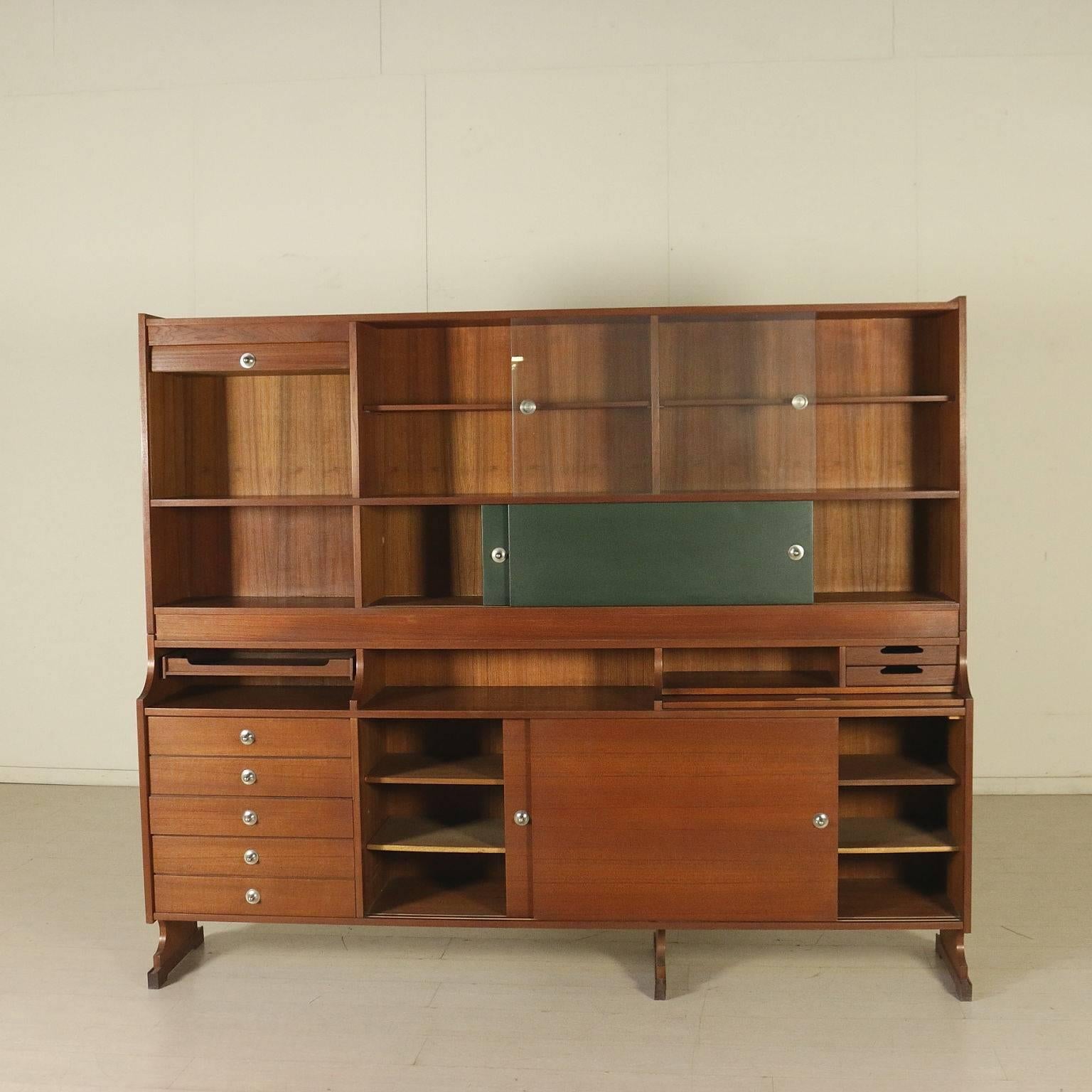 A cabinet with raised top and sliding doors, drawers and extractable writing top. Teak veneered wood, glass, leatherette upholstery. Manufactured in Italy, 1960s.