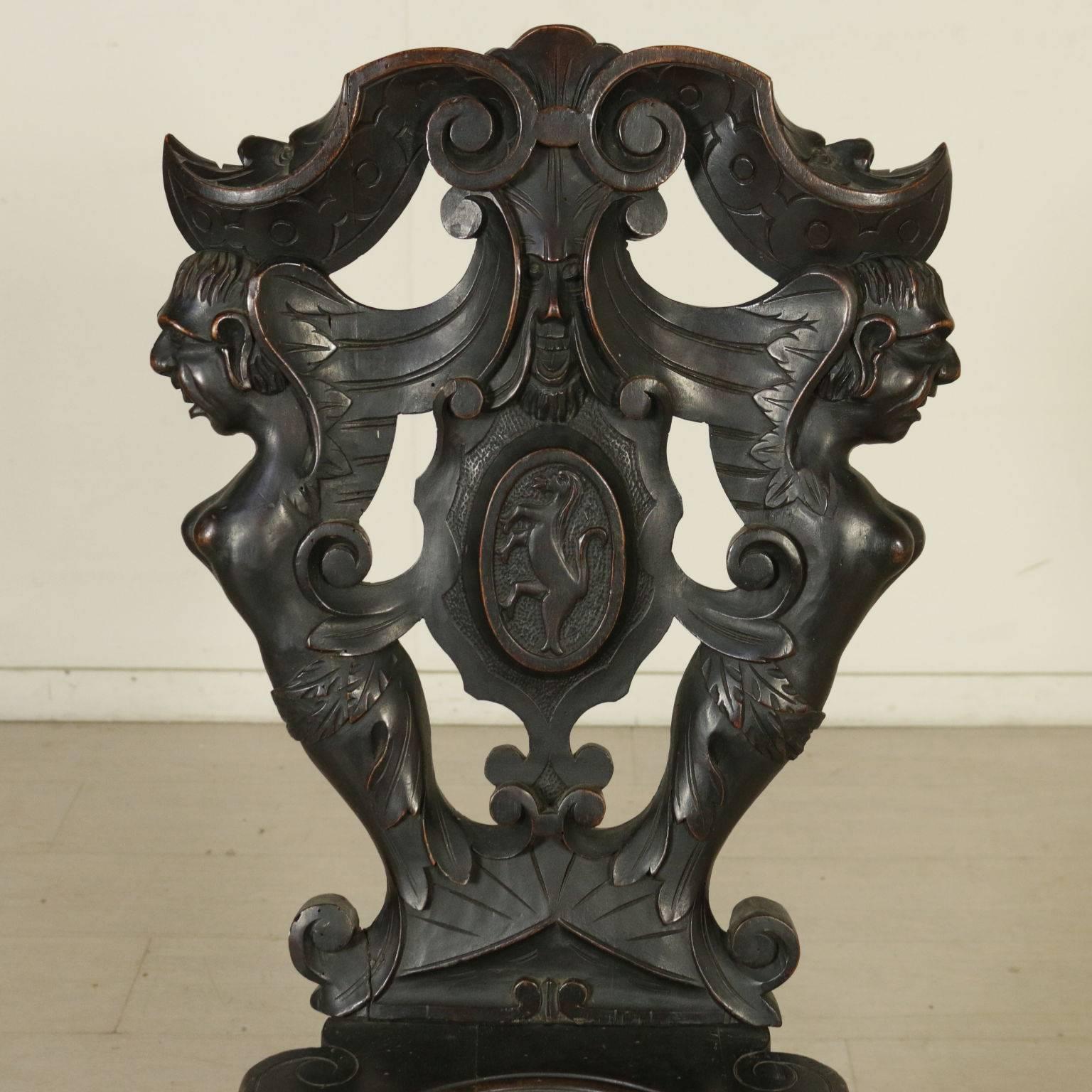 Renaissance Revival pair of walnut chairs. They feature inlaid legs and a richly carved backrest with leaf motifs, masks and family coat of arms. Manufactured in Italy, early 20th century.