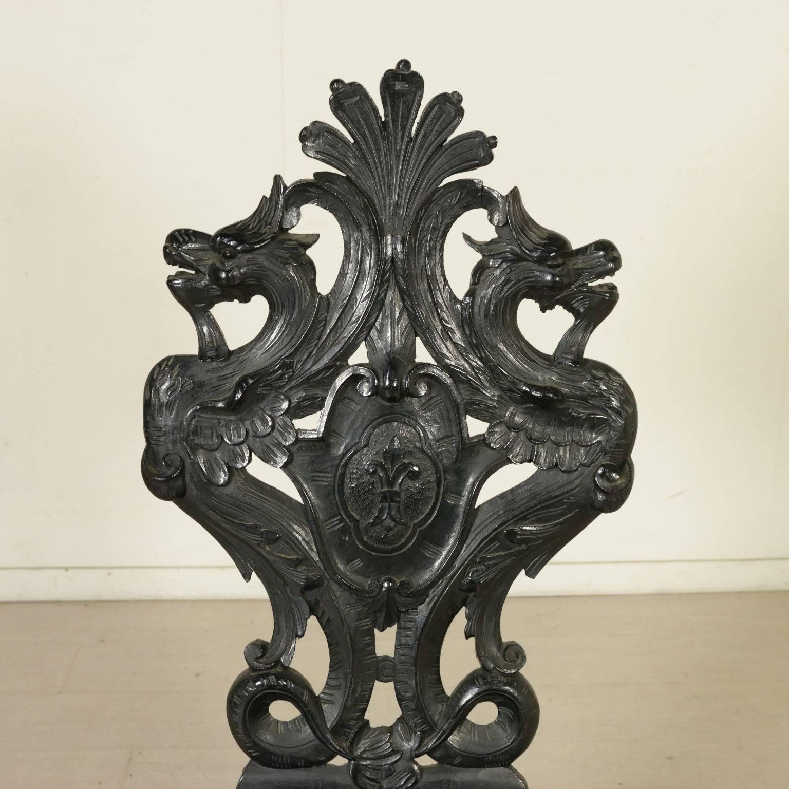 Renaissance Revival style pair of walnut carved chairs. They feature richly carved front legs and backrests. Perforated with masks, dragons and central coat of arms. Manufactured in Italy, early 20th century.