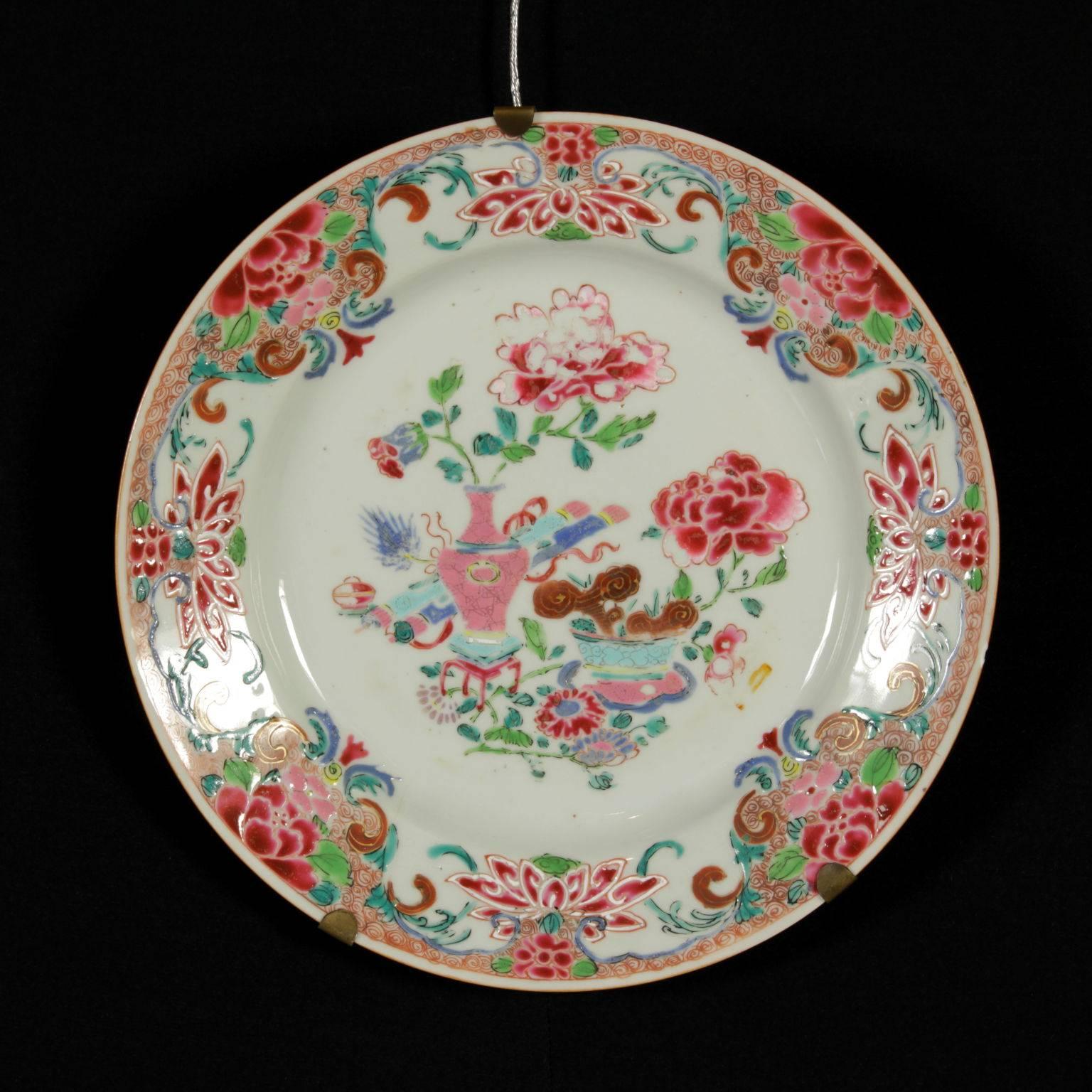 A group of six 'Famille rose' plates made of Chinese porcelain decorated with polychrome glazes. In the middle, a composition with an ancient vase full of peonies, two rolls and a vase with Lingzhi mushrooms. The perimeter is decorated with