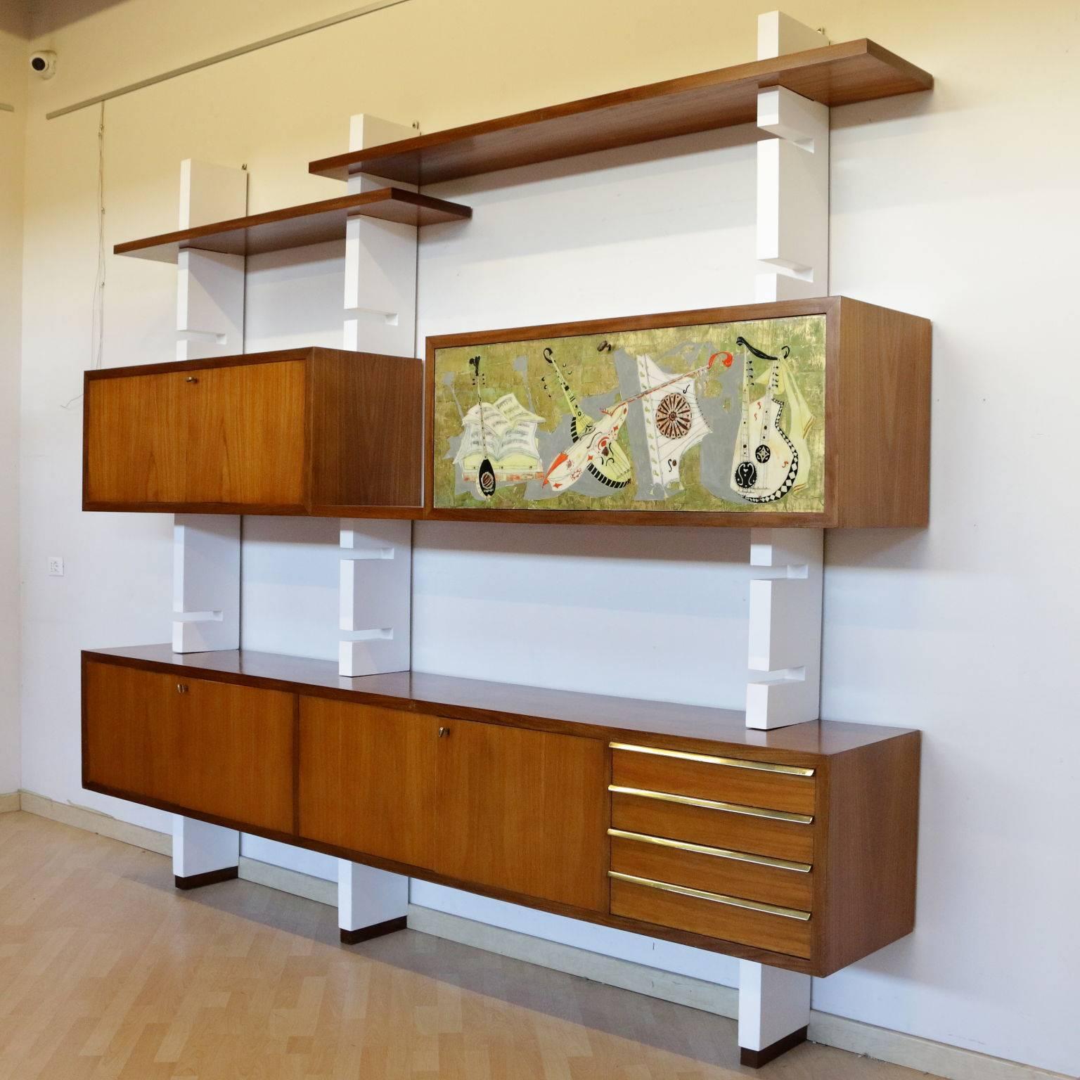 A bookcase with open shelves and containers. Mahogany veneer, lacquered wood uprights, brass and a drop-leaf door with silk-screened drawing. Manufactured in Italy, 1960s.