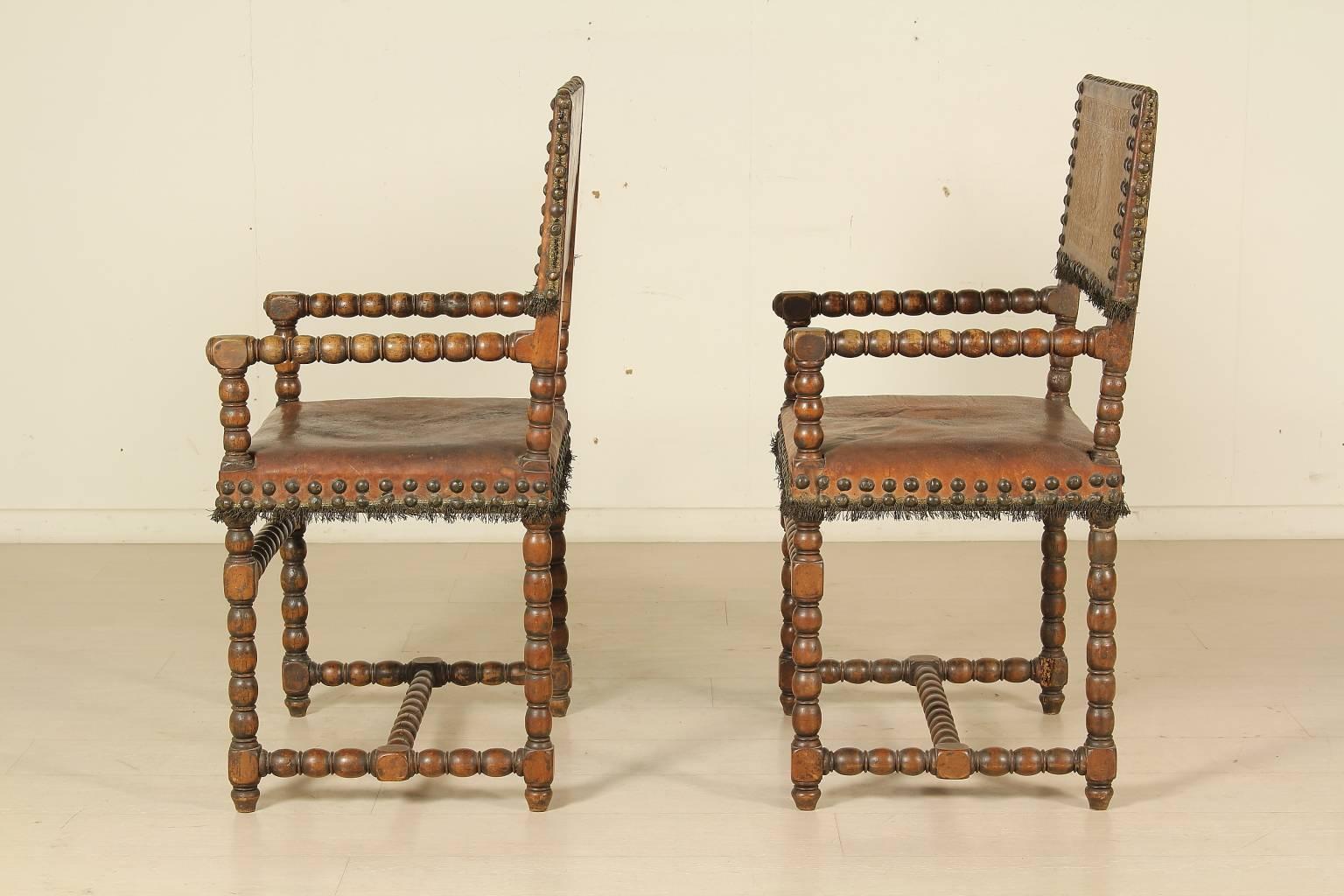 Two Renaissance 17th Century walnut and leather armchairs. Sphere-turned walnut wood, also on the armrests. Studded leather seat and backrest. On the backrests, the leather has got pressed arabesque and grotesque decorations on a gilt background.