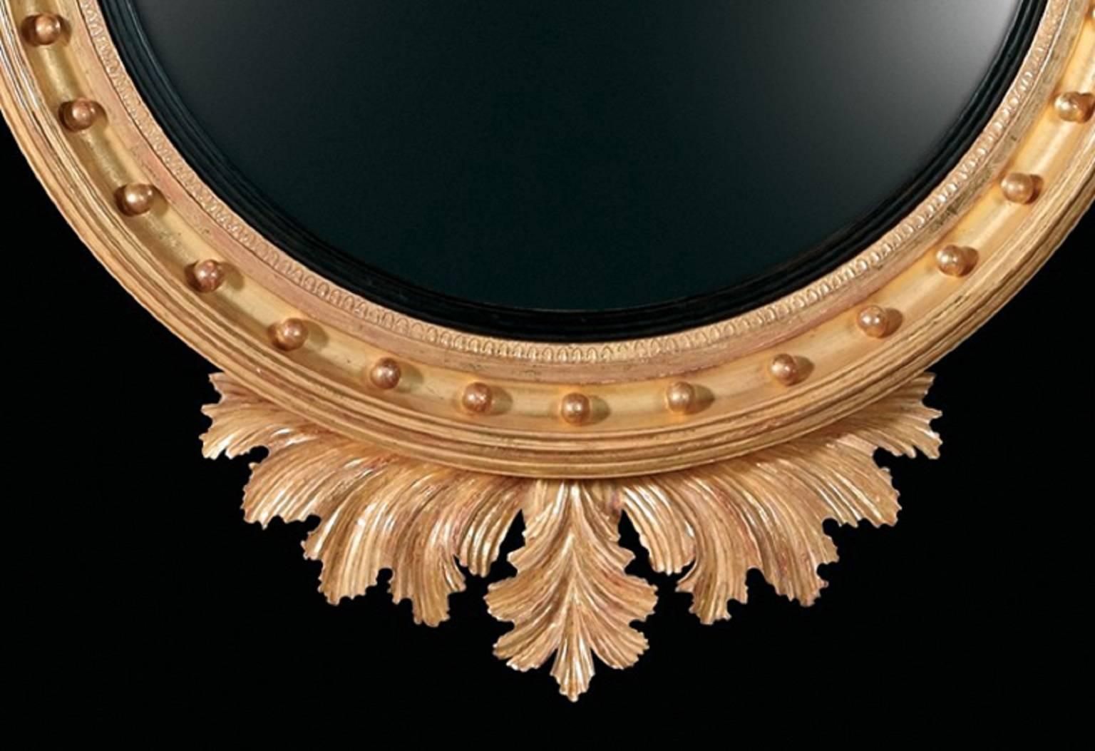 A Regency style carved giltwood round / circular convex looking glass mirror with ebonized inner slip and ball decorated moulded frame. The ebonized eagle cresting sits upon a tapered and reeded plinth flanked by scrolling acanthus leaves and with a