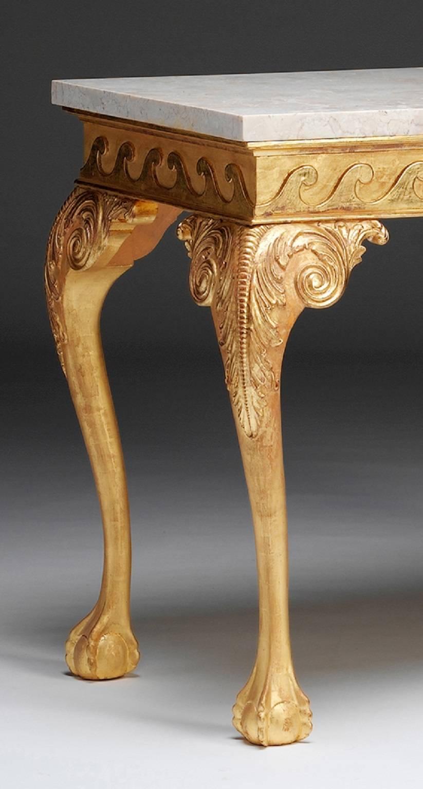 A carved giltwood side table in the George II tradition. The rectangular marble top sits above a Vitruvian scrolled frieze raised on a cabriole legs. The legs are carved with acanthus leaf capped knees and with scrolled and leaf carved ear brackets