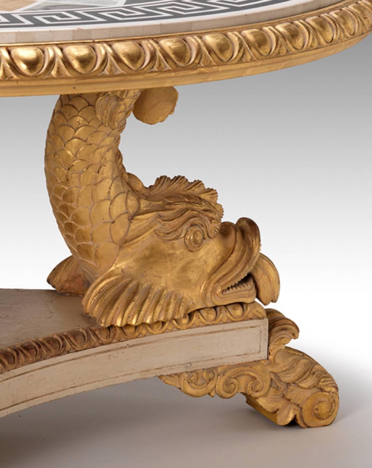 A fine Regency design circular centre table with inset marble geometric inlaid top within an egg-and-dart frieze supported on three carved stylized dolphins resting upon an aged gessoed triform base with gilded wood carved foliate feet.

This item