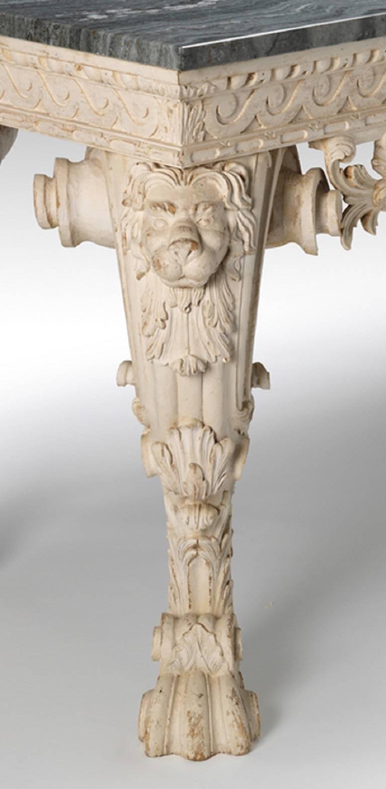An exceptional pair of carved and aged painted tables with marble tops above an egg-and-dart Vitruvian scroll frieze centred by scrolling acanthus leaf ‘C’ scrolls and rocaille flanked by pierced scrolling cabriole legs with lion mask carved at the