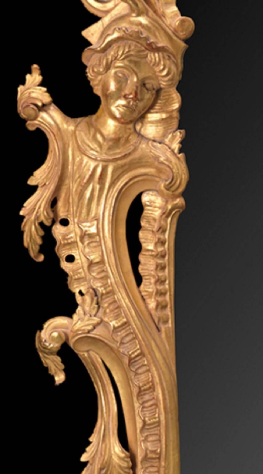 The carved gilt-wood frame with central mirror plate flanked by caryatides issuing from foliate scrolls to the sides, with addorsed ‘C’-scrolls to the base, the wing spandrels dressed with icicle waterfalls within a framework of asymmetrical ribbed