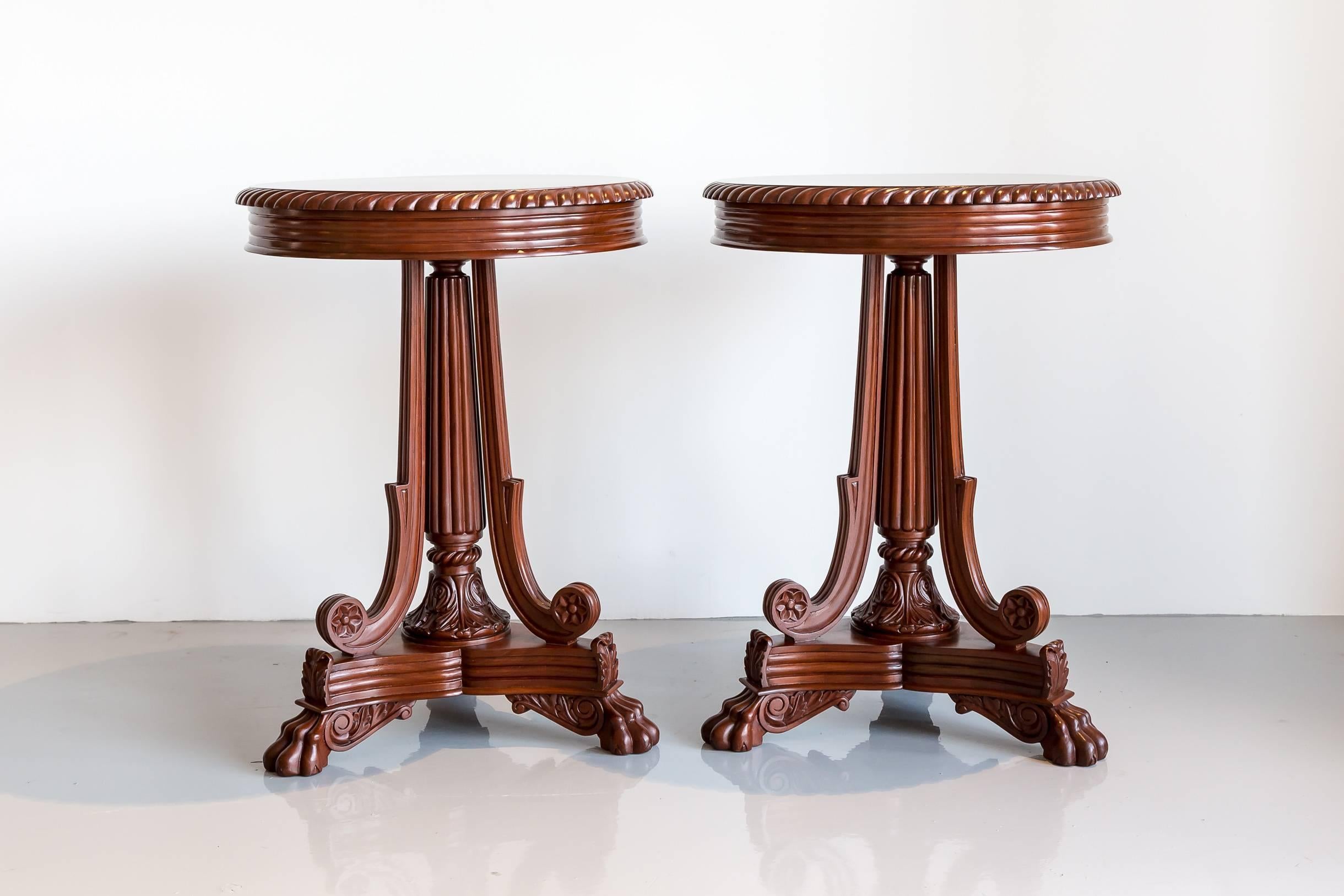 A pair of elegant British colonial round side tables made of mahogany. The round top with a gadrooned edge rests on a reeded column and three curving supports ending on a flat and craved tri-form base with paw feet.

The tables were found in