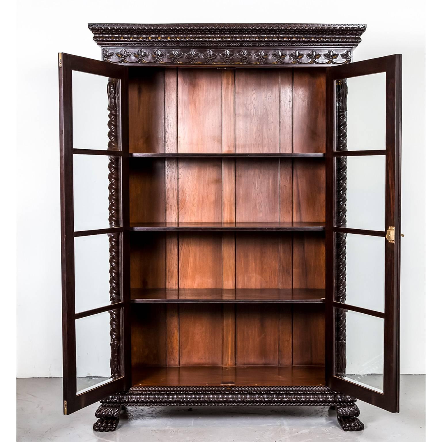 A magnificent British Colonial glass front cabinet in rosewood with a deep cornice consisting of a wide band of floral carving and egg and dart carving on the edge. The frieze is relief carved in a pattern of fleur-de-lys. 
The cabinet has double