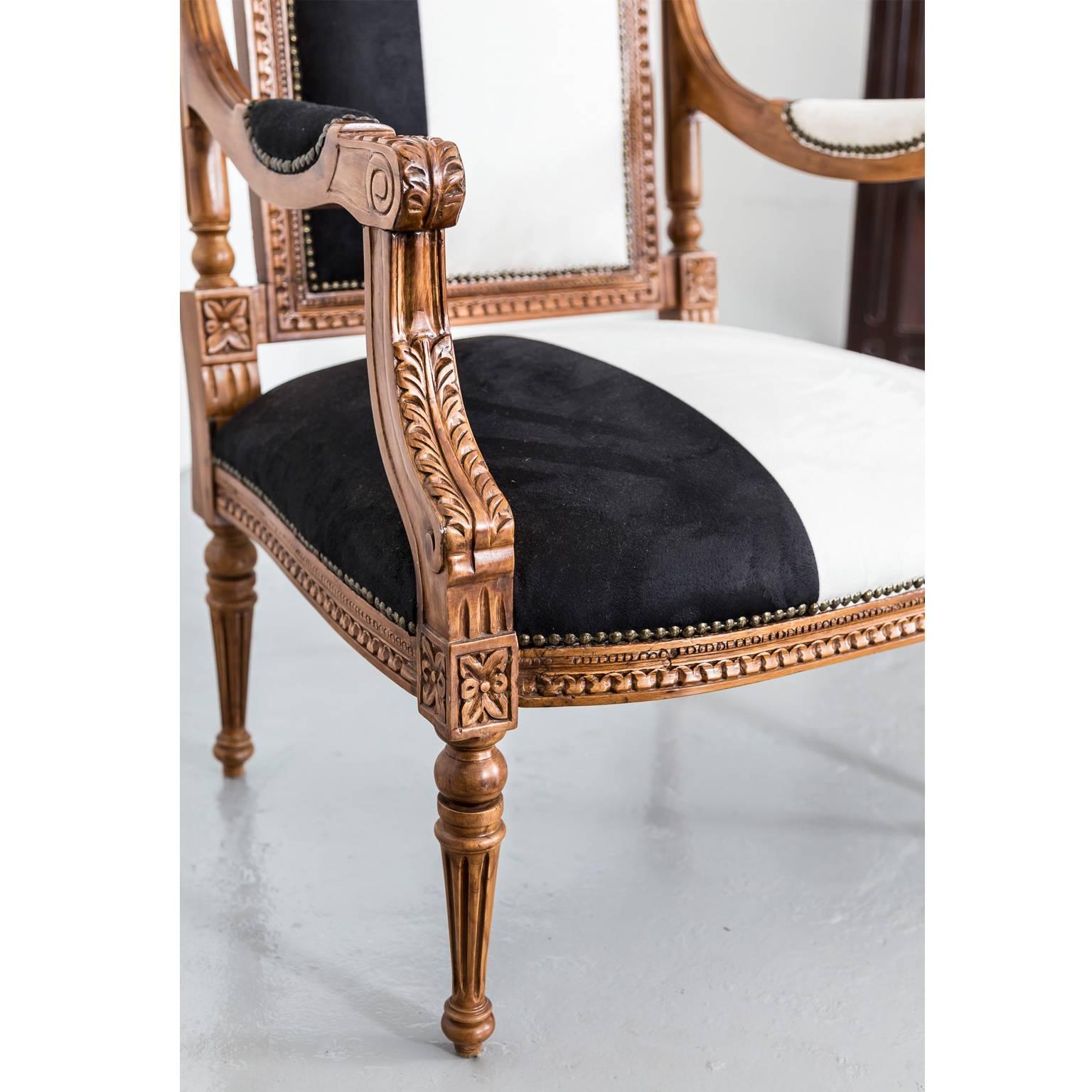 A pair of British colonial open armchairs in Louis XVI style. 
The high back consists of a central upholstered panel that is surmounted by a shaped top rail, pierced and carved at centre with a floral design. Each upright supports a small finial