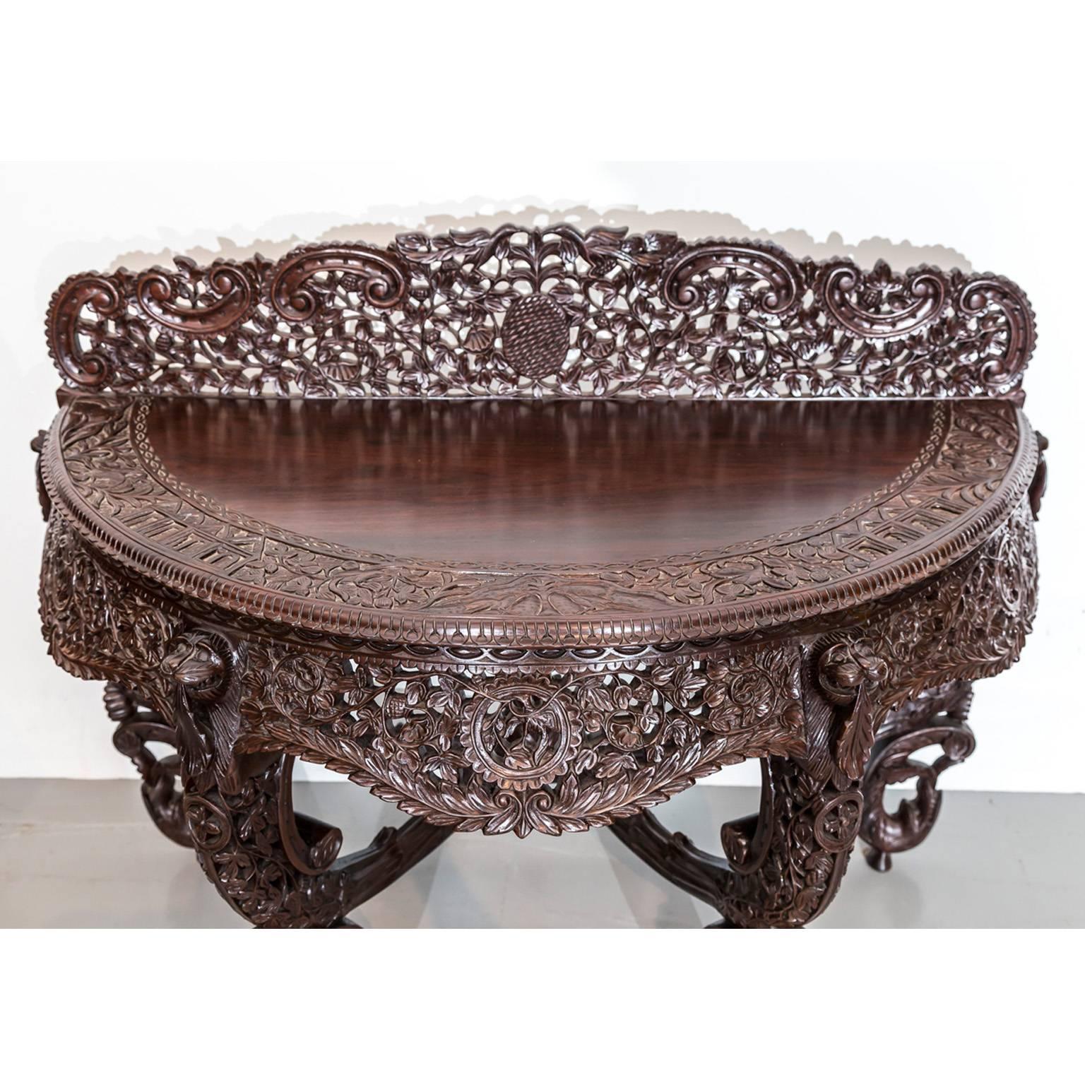 A highly decorative British Colonial rosewood console table supported by four profusely carved legs terminating into monkey faces at the table top. 
The top consists of a fine figured piece of rosewood and a broad band of richly carved foliage