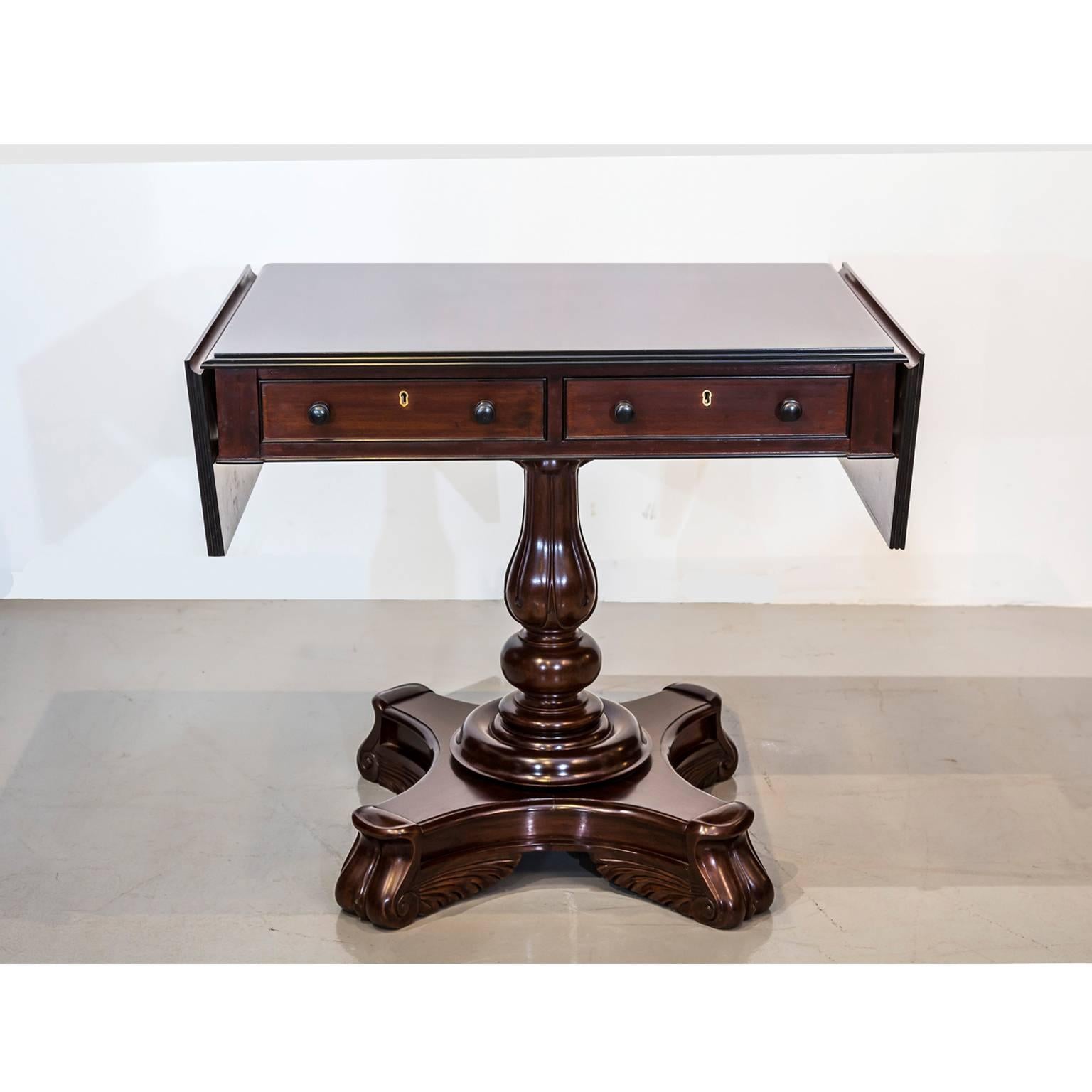 A British Colonial mahogany drop-leaf table with a central pedestal.
The overhanging tabletop has reeded edges and is mounted at either side with a drop-leaf which is secured with brass hinges. When raised, each leaf rests on a bracket, even with