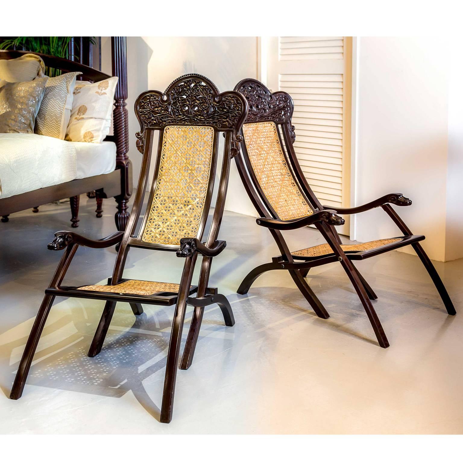 A pair of Portuguese colonial rosewood folding chairs. Each chair is composed of three components joined with steel screws; the back, the seat and arms, each extends down to form one of the three pairs of legs. 
The back is concave with a carved
