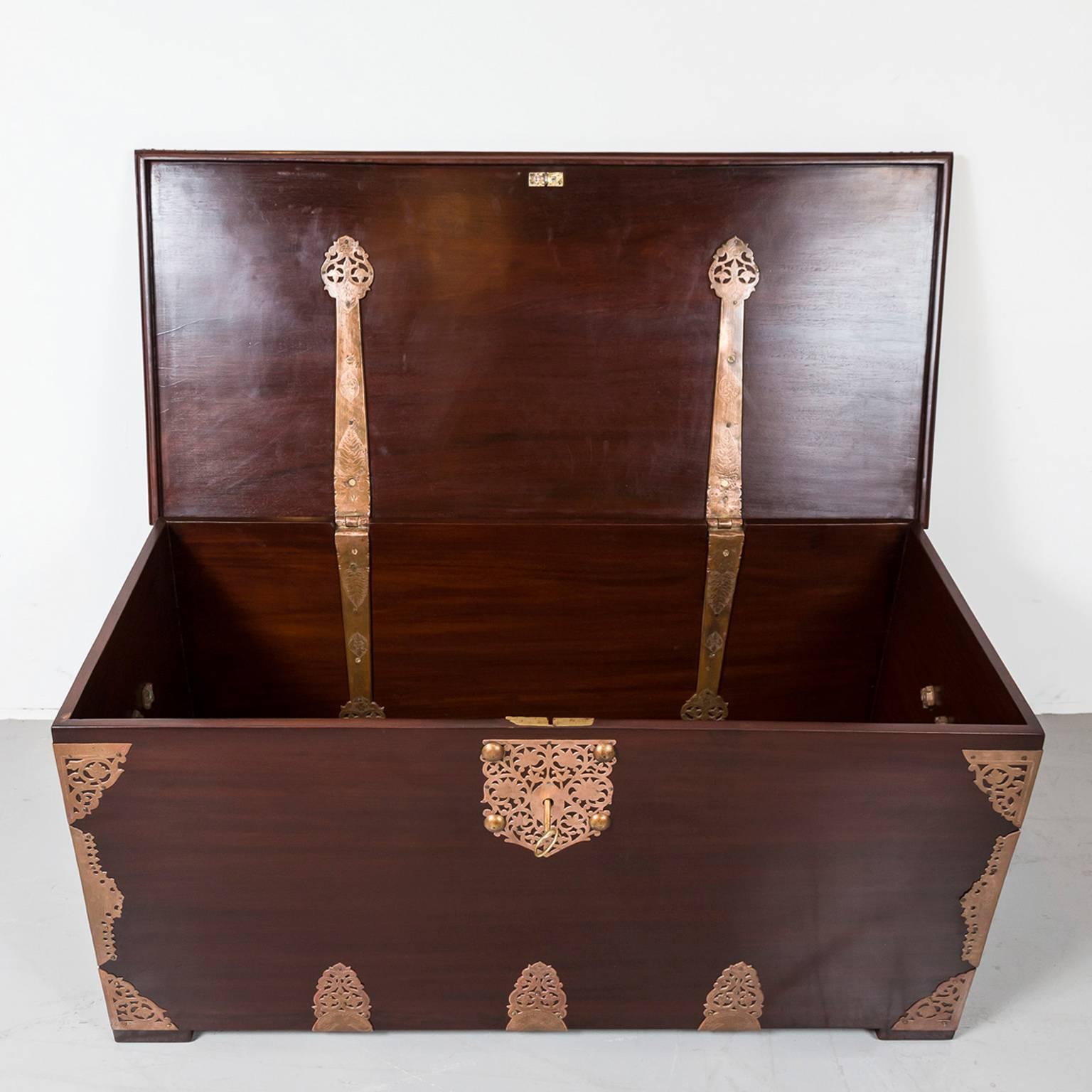 A beautiful Dutch colonial storage chest of solid plank construction in mahogany. It incorporates both Mughal and Dutch influences. 
The chest is strengthened and simultaneously ornamented by open work brass mounts on the sides, corners and bottom.