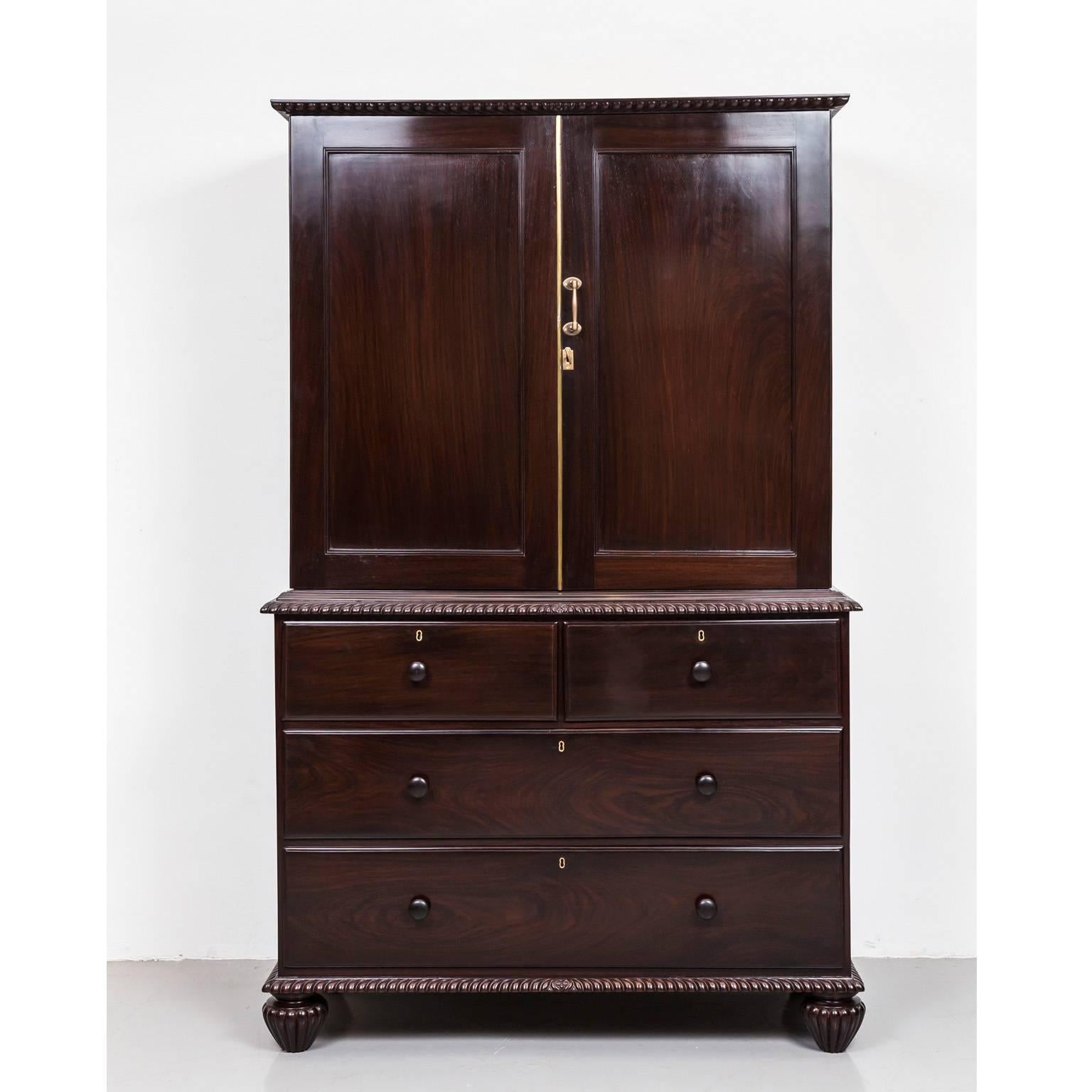 A top quality British colonial cupboard made of rosewood. The upper section has a flat top with egg and dart carving on the frieze and paneled doors. 
The interior in mahogany and is fitted with three sliding shelves. The lower part comprises two