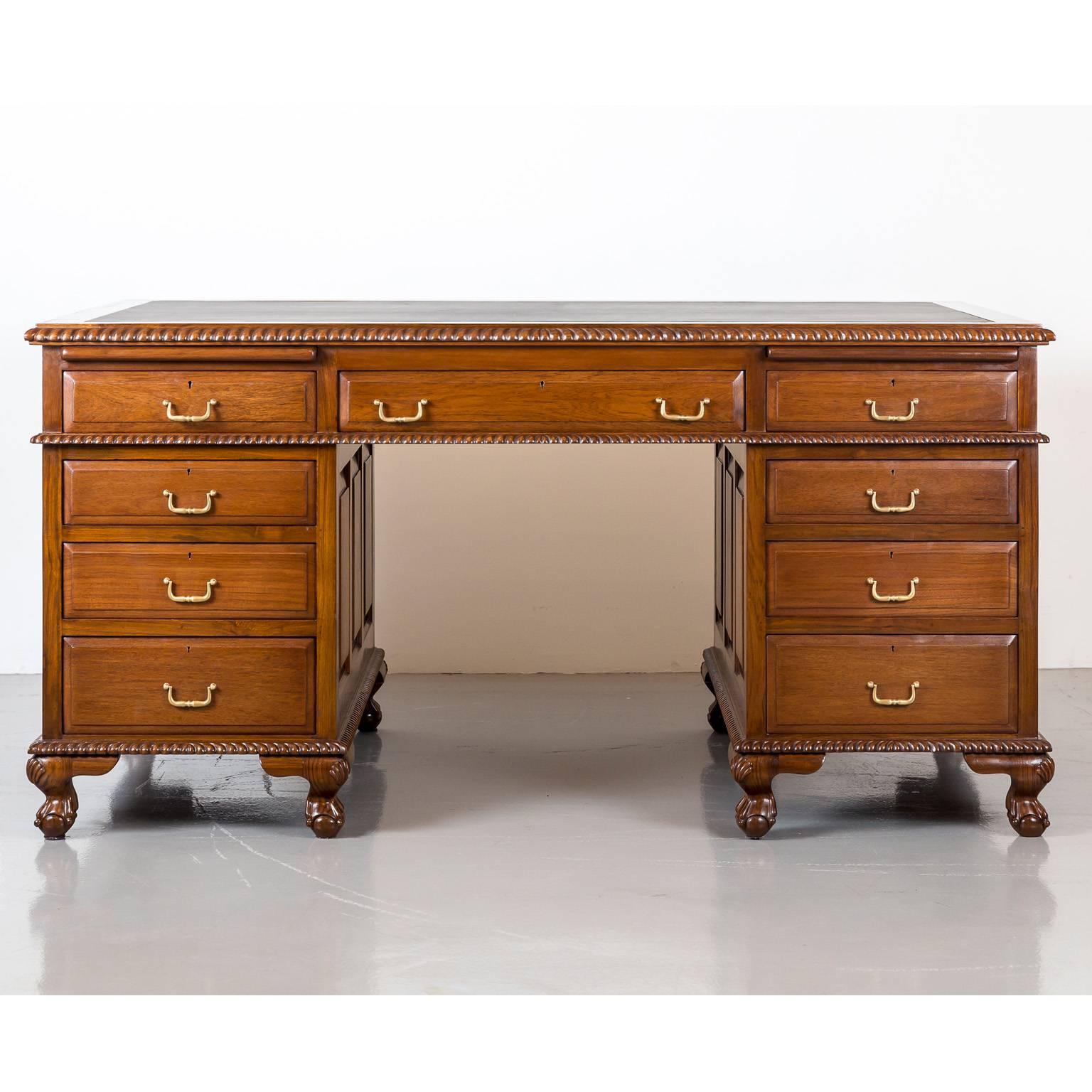 An impressive British Colonial twin pedestal desk in teakwood with a large overhanging top above a central knee hole. The top with a black leather writing surface consists further of a central drawer flanked by two smaller ones. Each pedestal has