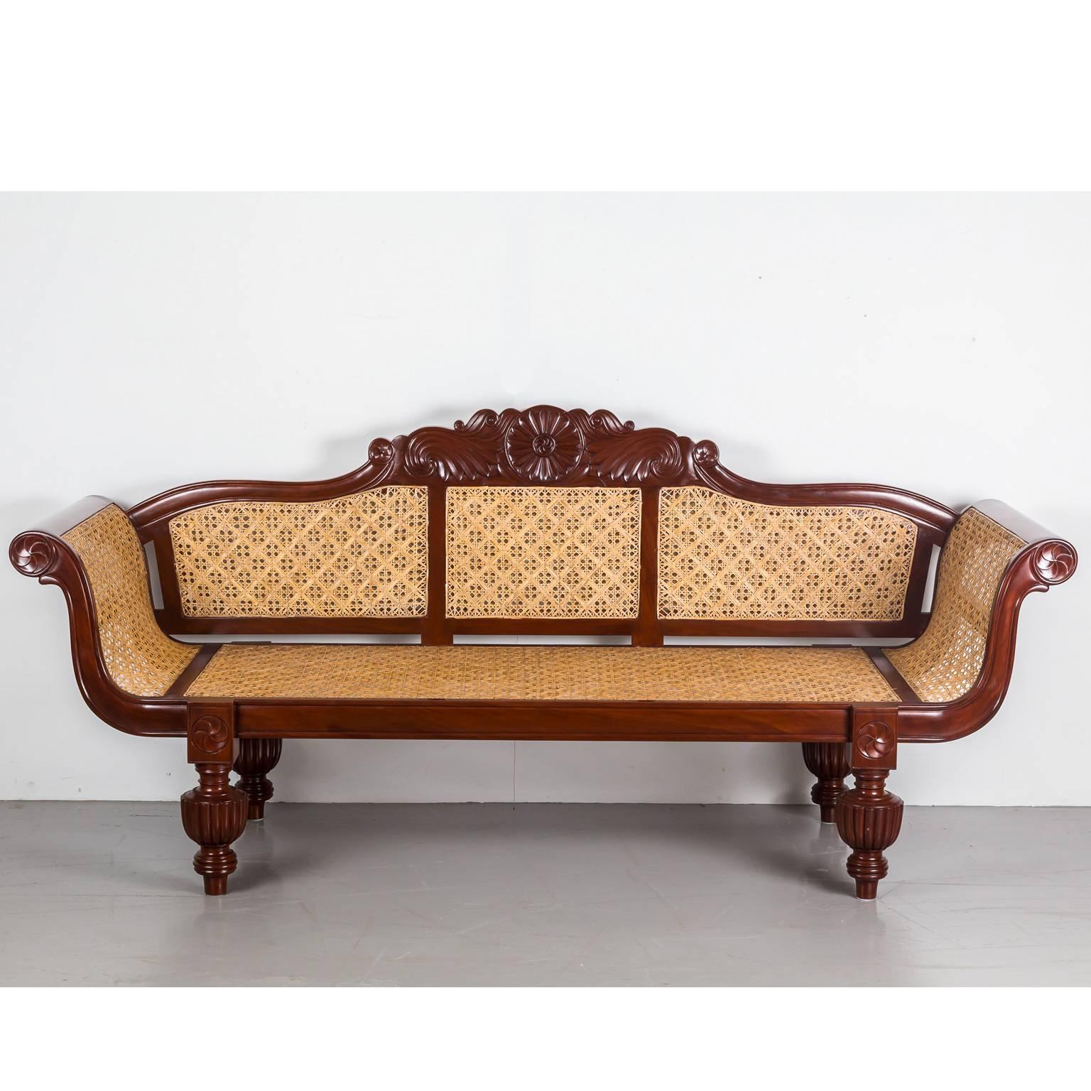 A nice British colonial sofa in mahogany with an arched serpentine crest rail centred by a floral carving. 
The back features three inset caned panels above a caned seat. The scrolled arms also display finely carved floral designs on the ends; a