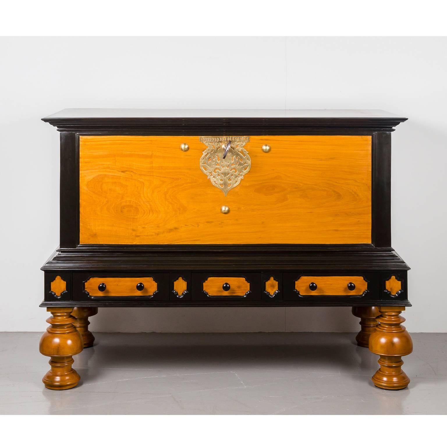 A stunning, large Dutch colonial storage chest of solid plank construction in satinwood, the lid and panels surrounded by an ebony edge. 
The front features an elaborate pierced brass escutcheon with original lock and large key and is further