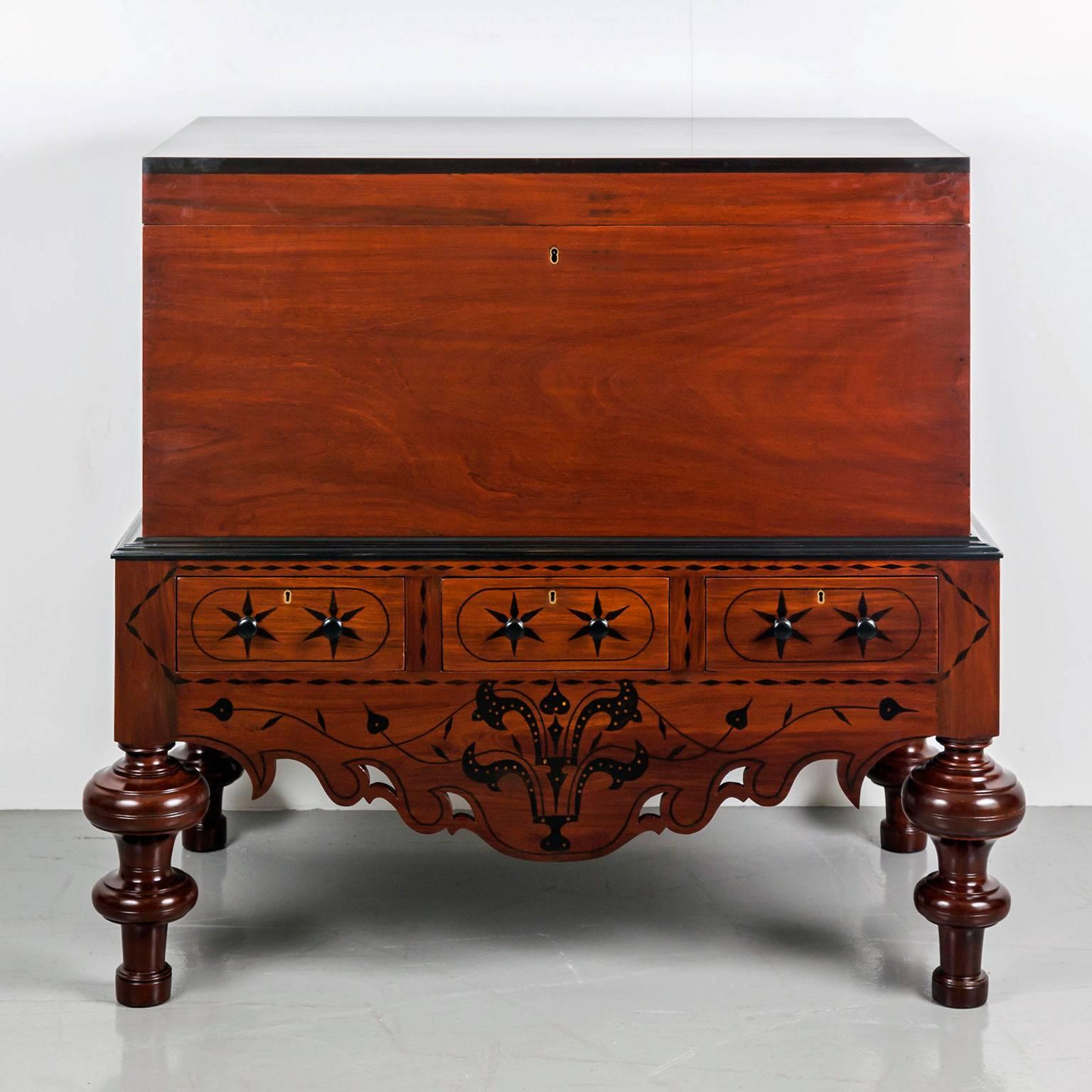 A typical Dutch colonial mahogany chest on stand of solid plank construction. The hinged cover with a molded ebony edge opens to a plain interior. 
The chest rests on a stand with a deep apron, the short sides and back are rectangular. The front