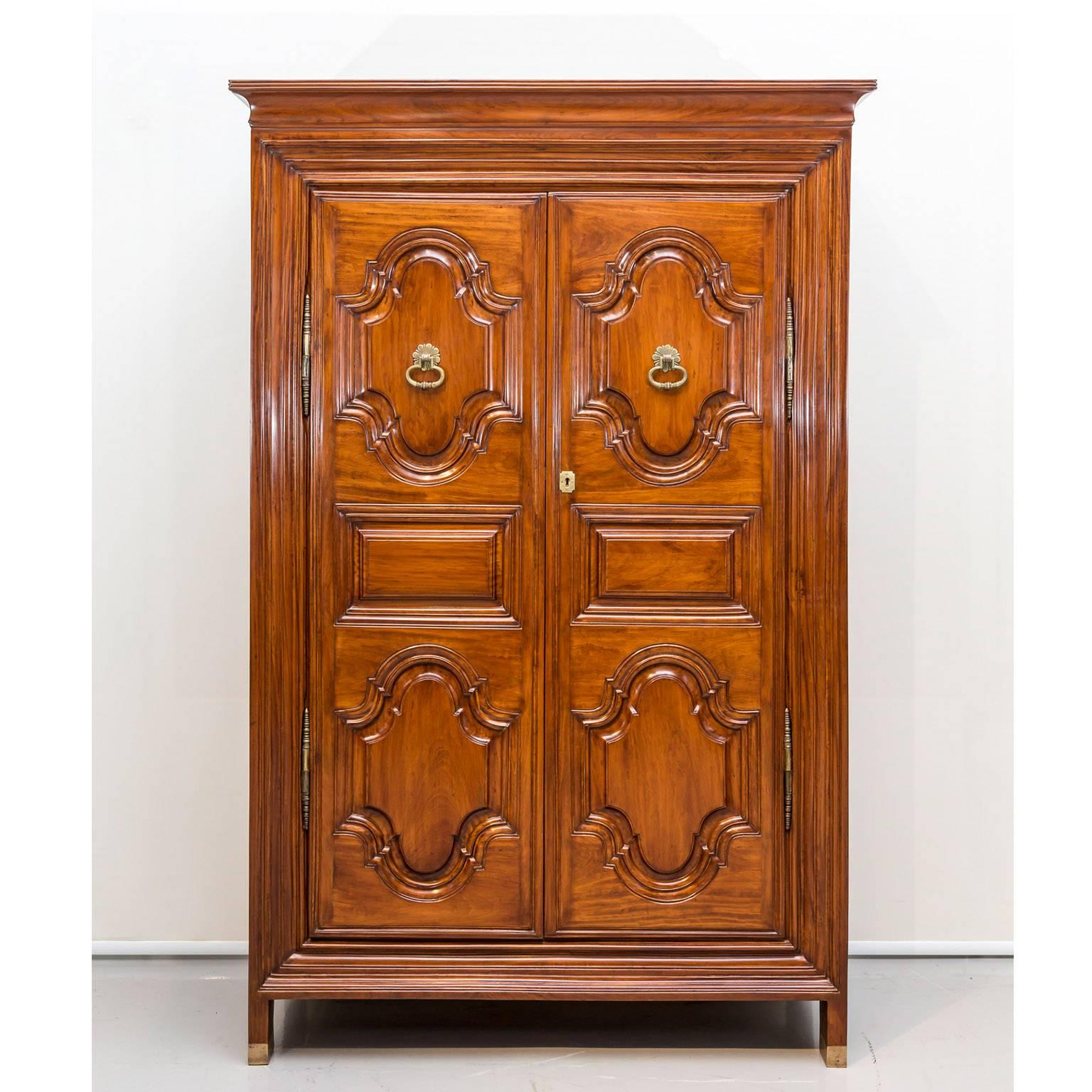 A unique Dutch colonial satinwood cupboard with a flaring cornice above a short frieze. The double doors are constructed with raised panels and feature decorative brass handles and unusual style hinges. 
Inside are two removable shelves.
The