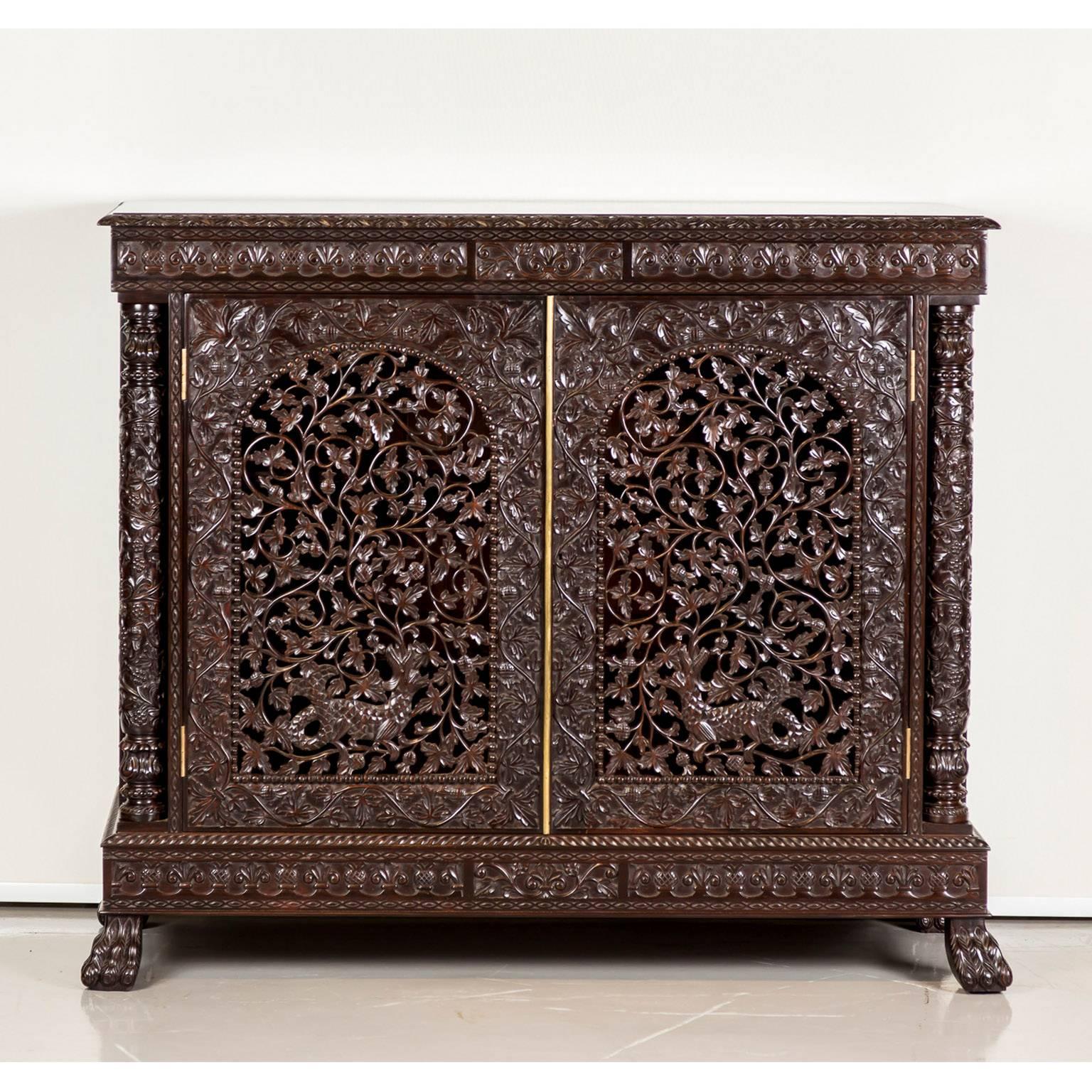 A beautifully carved British colonial cabinet in rosewood. The overhanging top is made of one piece of rosewood with a carved border. The front is mounted with hinged doors that are intricately pierced and relief carved with an intertwining floral