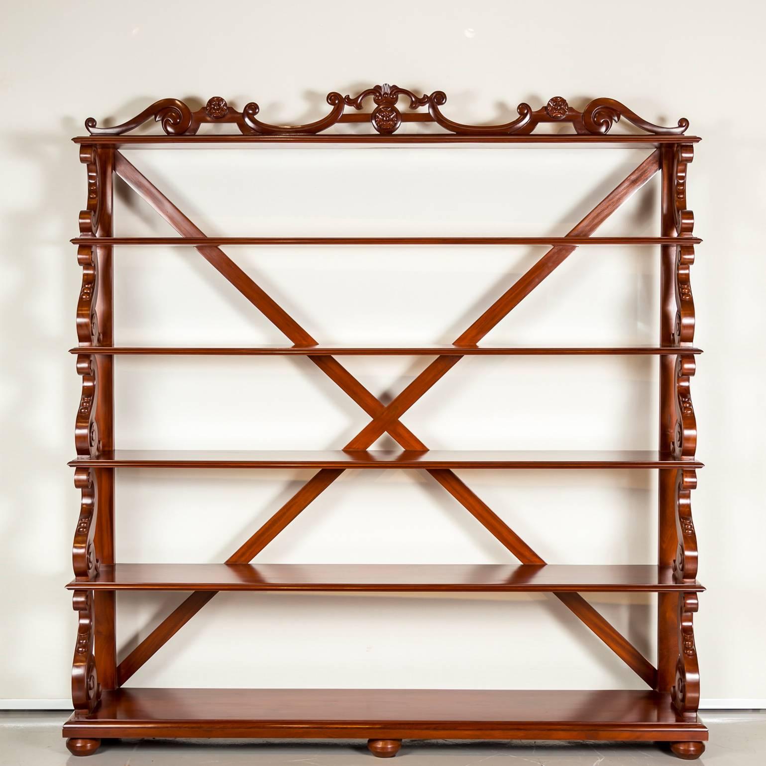 A large British Colonial ‘waterfall’ open bookcase in mahogany with six graduated shelves. The shelves are supported and connected by solid S-shaped stretchers. 
The top shelf decorated with a nicely carved gallery. The bookcase is further