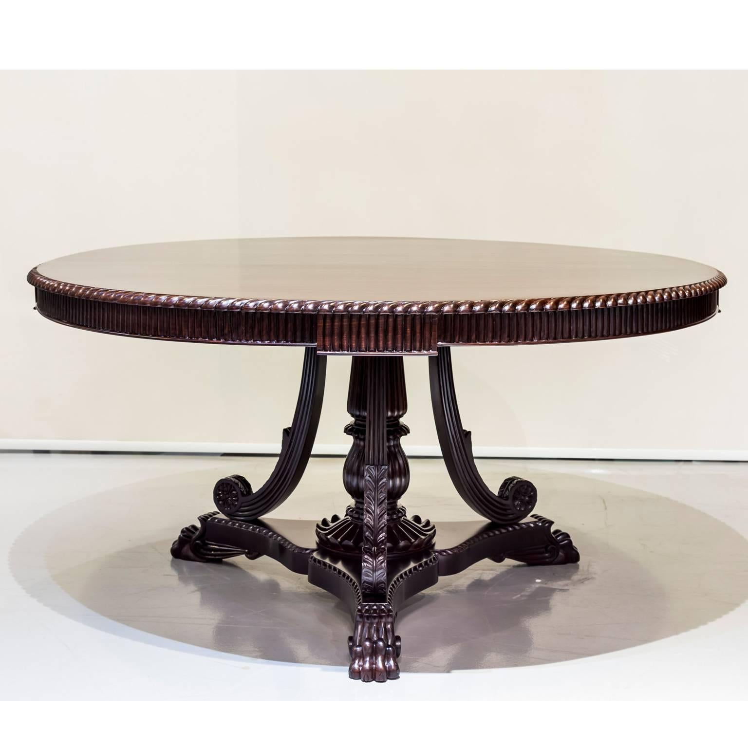 A beautiful British Colonial dining, or center table in rosewood.
The large circular top with gadrooning on the edge above the carved apron. It is supported on a column that is surrounded by three curved and scrolled spindles and rests on a flat