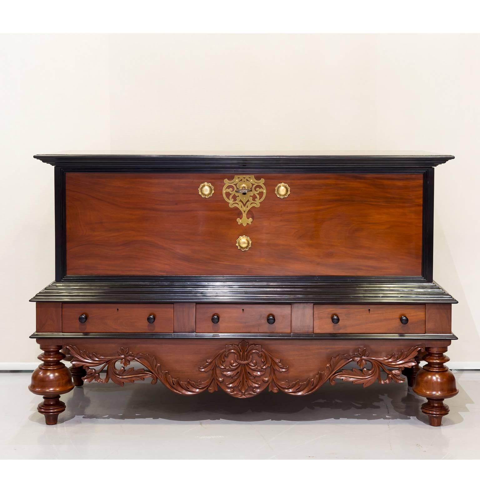 A stunning, large Dutch colonial storage chest of solid plank construction in mahogany; the lid and panels surrounded by an ebony edge. 
The front features an beautiful pierced brass escutcheon with original lock and large key. Two large brass
