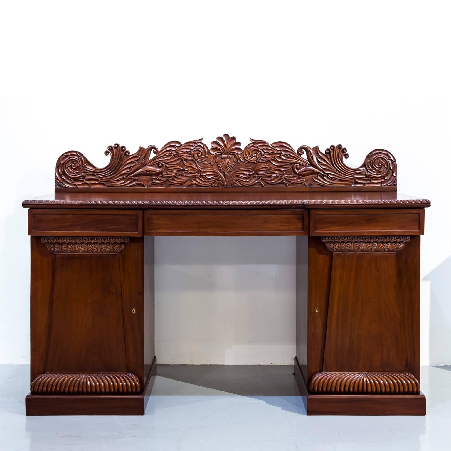 A fine Anglo-Indian mahogany pedestal sideboard.
The sideboard sits on two rectangular piers with hinged doors that open to an interior with one central shelf. The paneled doors with nice decorative carving. The top of the sideboard has an edge