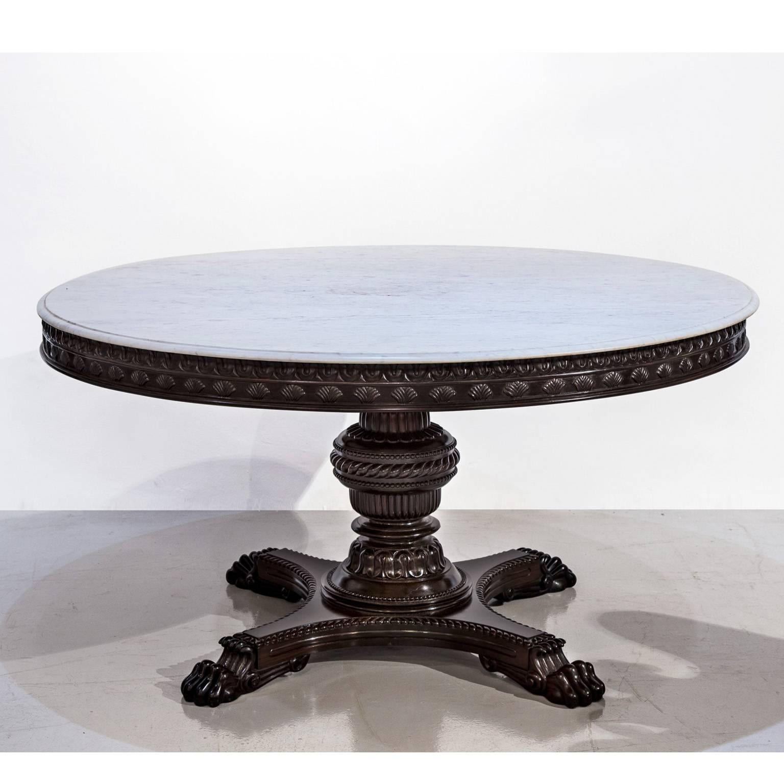 A British Colonial rosewood dining or center table with a marble top above a nicely carved apron. The baluster center support is well turned, beautifully carved and rests on a quadro-form base with claw feet.

The table was found at the Malabar