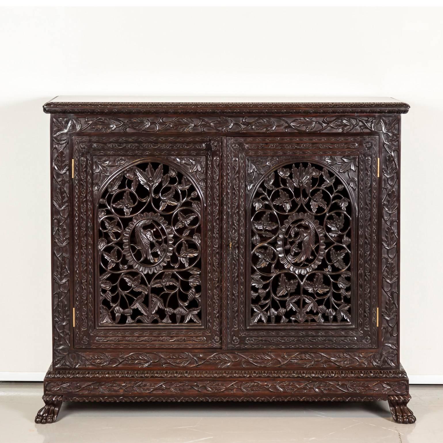 A fine, beautifully carved British colonial cabinet in rosewood. 
The overhanging top made of one piece of rosewood with a carved border. The front is mounted with hinged doors that are intricately pierced and carved with an intertwining floral