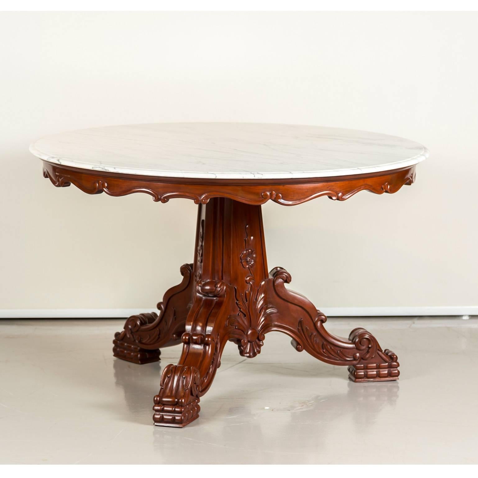 A British Colonial mahogany dining or center table with a new marble top. 
The circular top is beautifully figured with a carved and serpentine shaped apron. 
It stands on a solid and beautifully carved baluster support with three cabriole legs