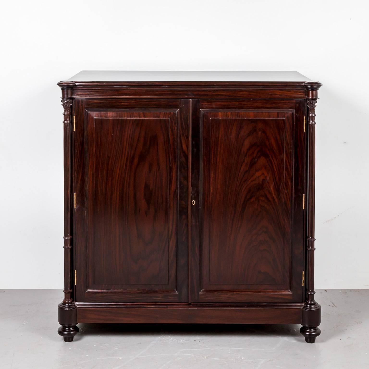 A British Colonial sideboard made of beautifully grained rosewood. The overhanging top is made of one piece of rosewood with rounded corners at the front. The double doors, which are constructed with fielded panels, are flanked by two carved solid