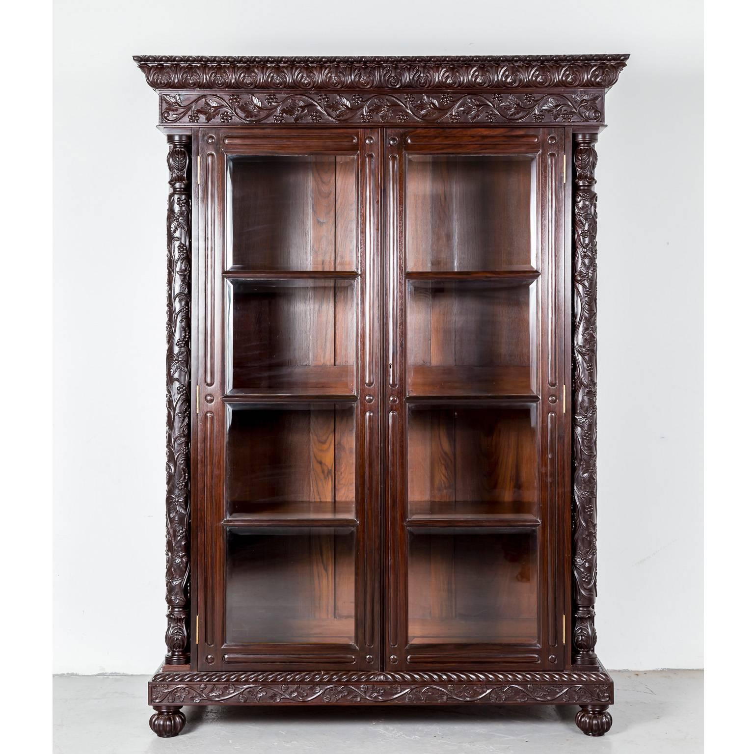 A magnificent British Colonial glass front cabinet in rosewood with a deep cornice consisting of a wide band of floral carving and egg and dart carving on the edge. The frieze is relief carved in an intertwining floral design. 

The cabinet has