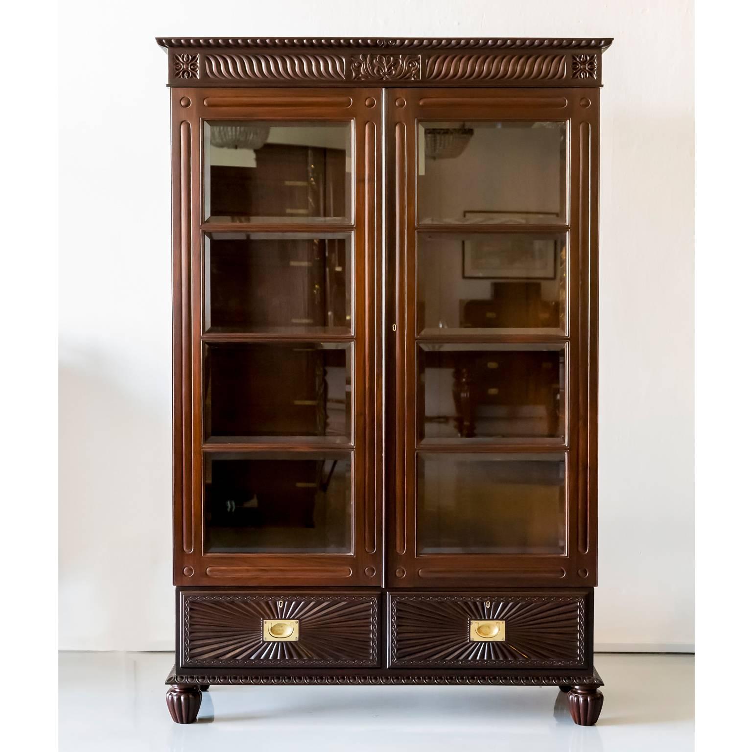 A beautiful British Colonial bookcase in rosewood with a flat top, gadrooning on the edge and wave carving on the frieze centred by a floral block.
The cabinet has double doors with eight beveled glass panels within a rosewood frame; they open to