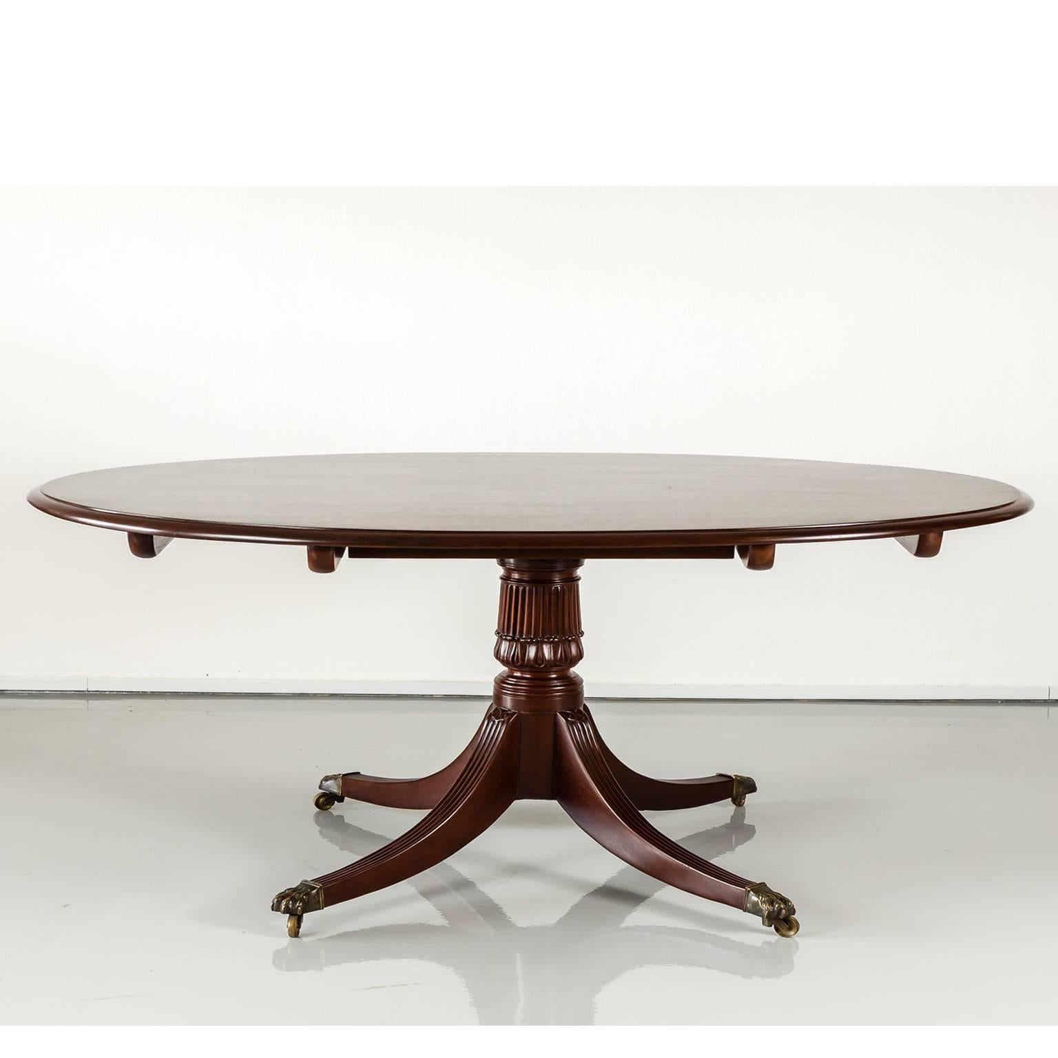 An elegant and unique Regency style single pedestal tilt-top dining table made of rare and beautiful Cuban mahogany. 
The oval top measures 156 cm x 106 cm (61½” x 41½”) and is made of a single plank(!). The solid base has a sophisticated carved