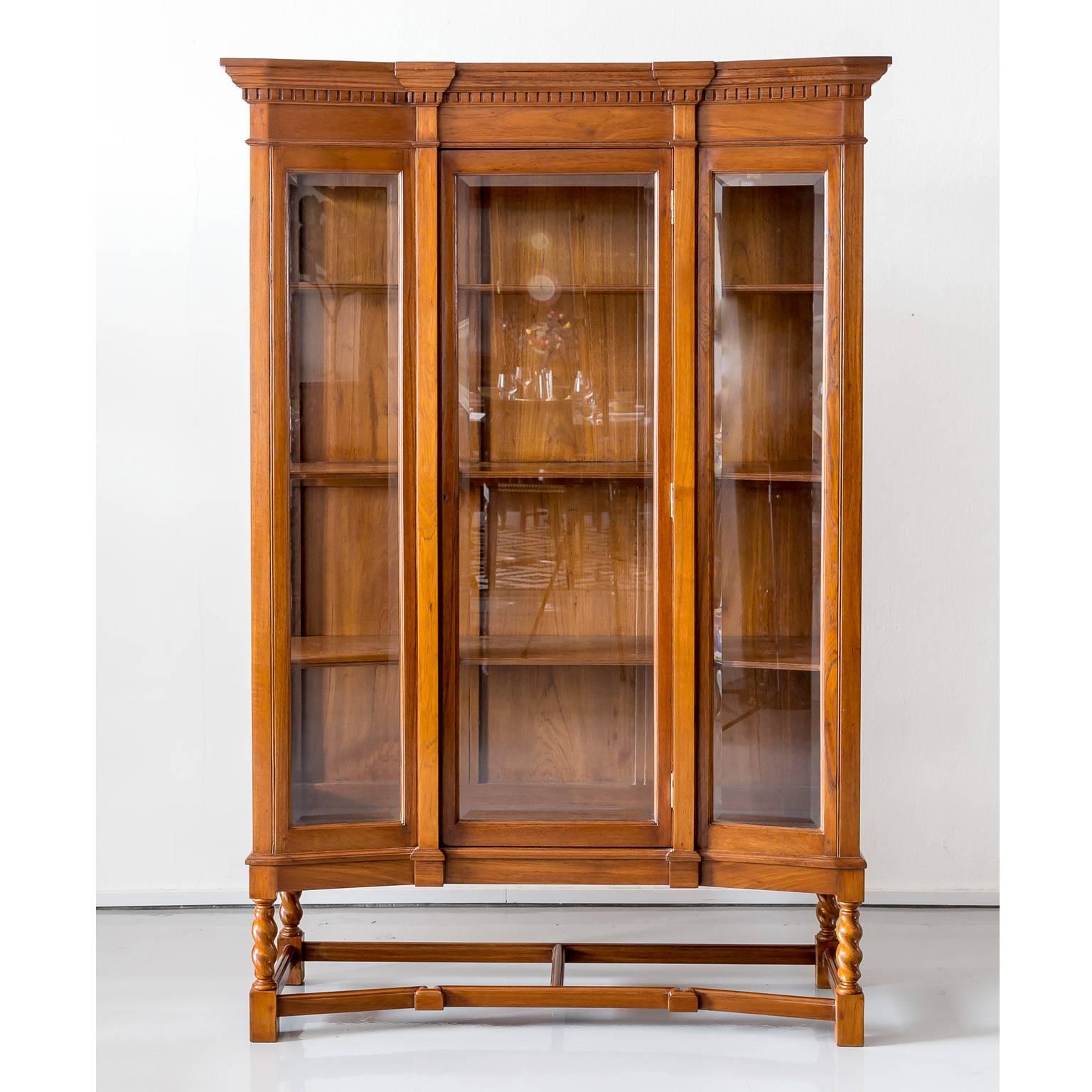 An elegant and serpentine shaped British colonial display cabinet in teak wood with
a deep moulded and carved cornice. The cabinet has one door with a large glazed
panel that is flanked by two pilasters and two smaller glazed panels. The two