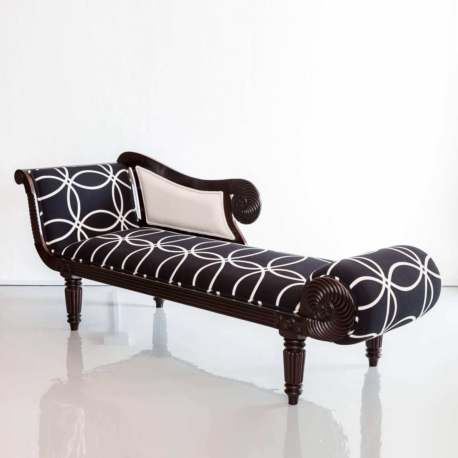 A British colonial rosewood récamier; a lighter daybed with scrolling end and footrest
decorated with carved designs along its frame.
The récamier is upholstered in black fabric decorated with white circles. A small neck-roll style pillow provides