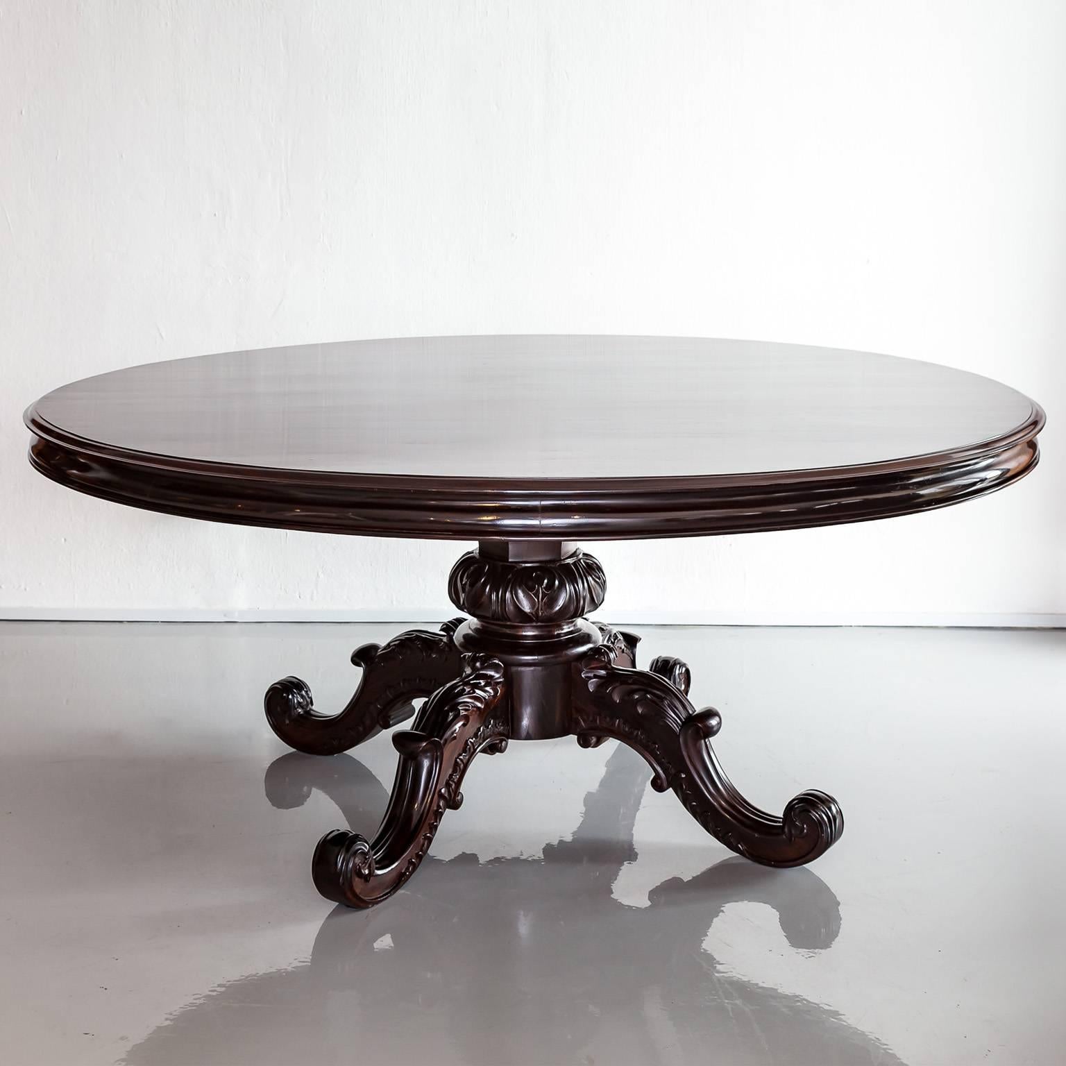 A beautiful, large British colonial round dining table made of rosewood. The circular top is superb with moulded edges above and below the apron. 
The solid base has a carved central pillar on a round platform which rests on four S-scrolled carved