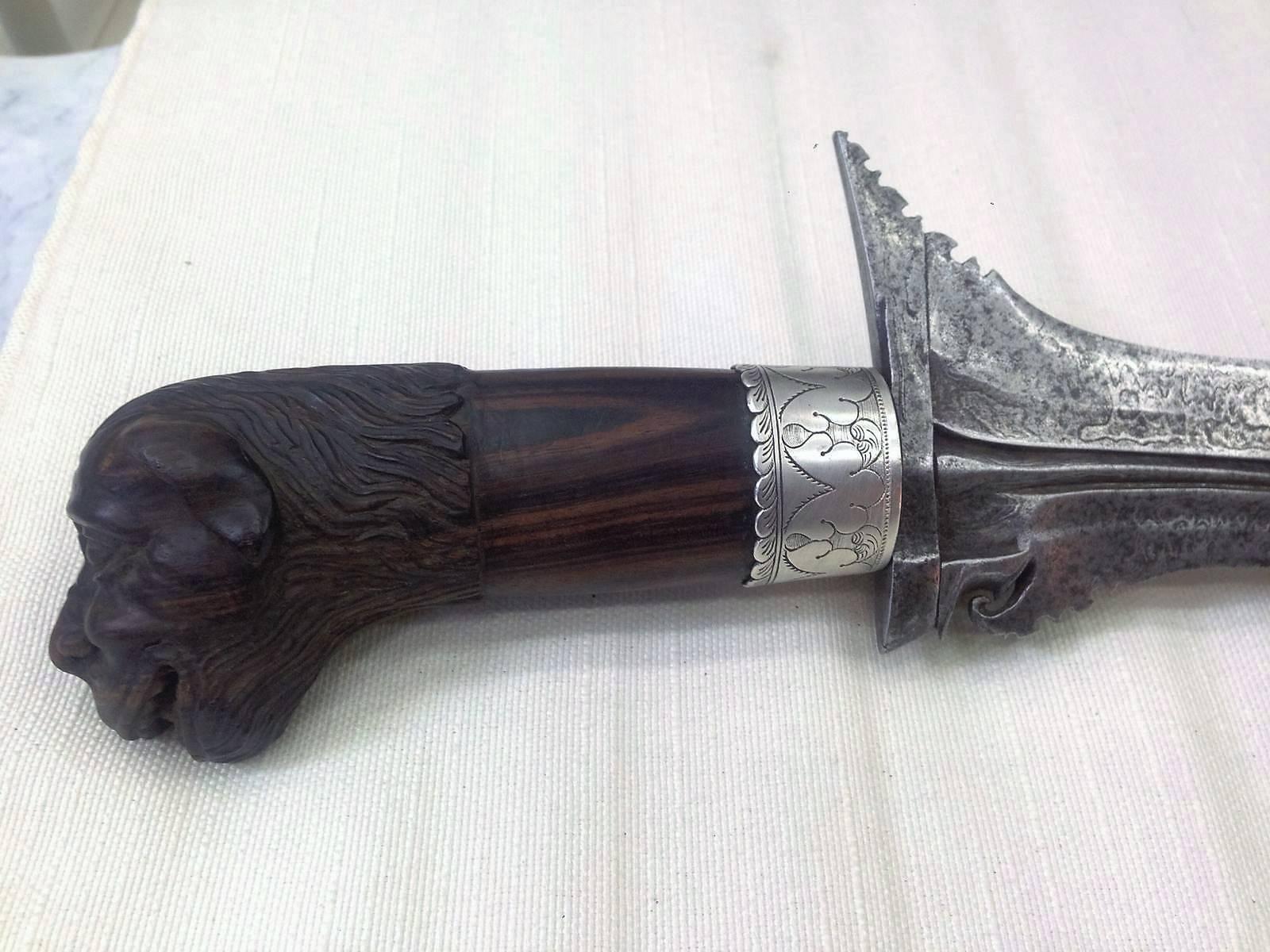 19th century sterling silver Malaysian Dagger.
Original carved mahogany wood handle.
Sterting silver carved crown.
Damascene steel.

The kris is an asymmetrical dagger with distinctive blade-patterning achieved through alternating laminations of